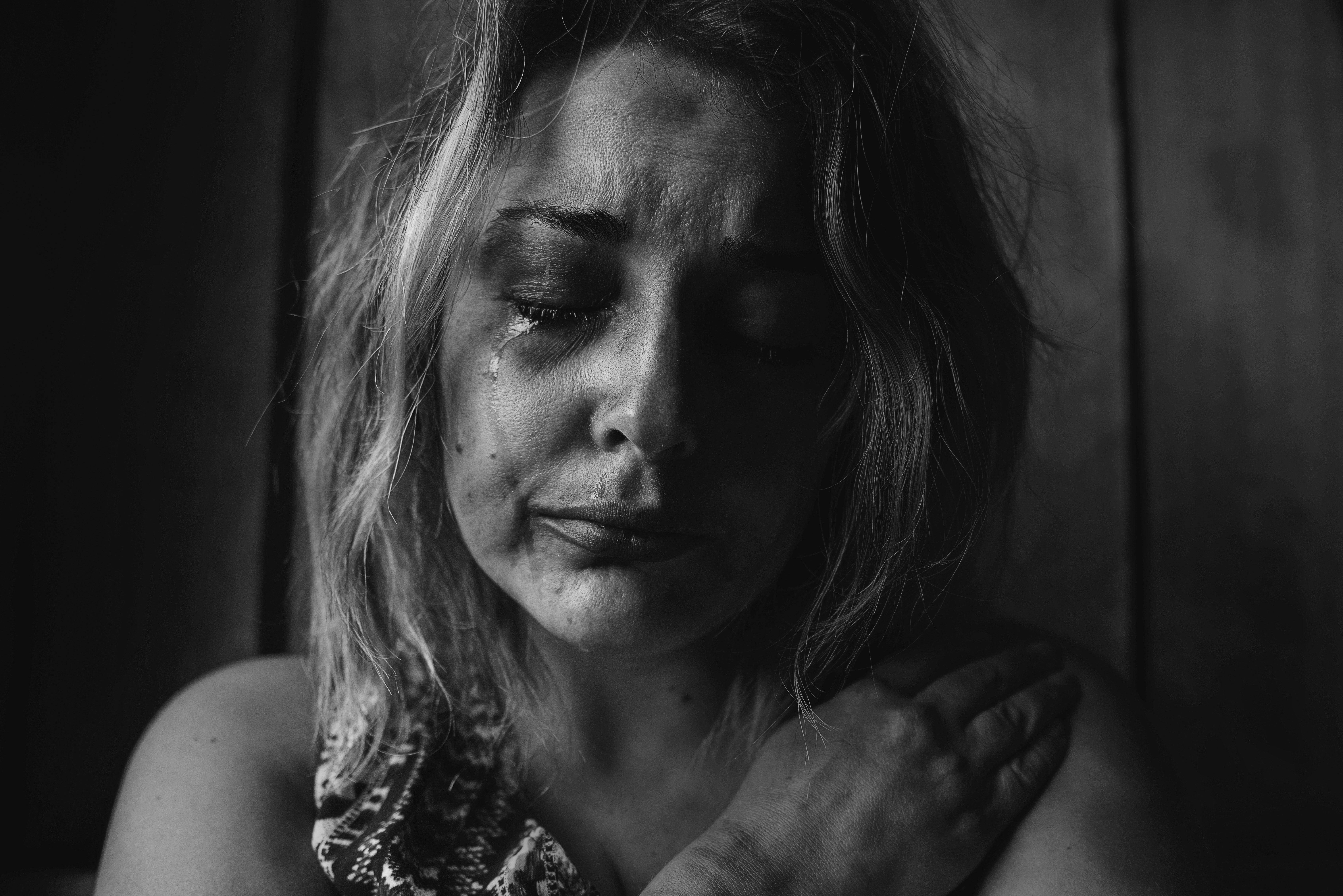 傷感少女黑白哭泣 壁紙 — 一個黑白肖像，一位臉上帶有淚痕的女人在昏暗的房間裡輕輕地抱著自己的肩膀。