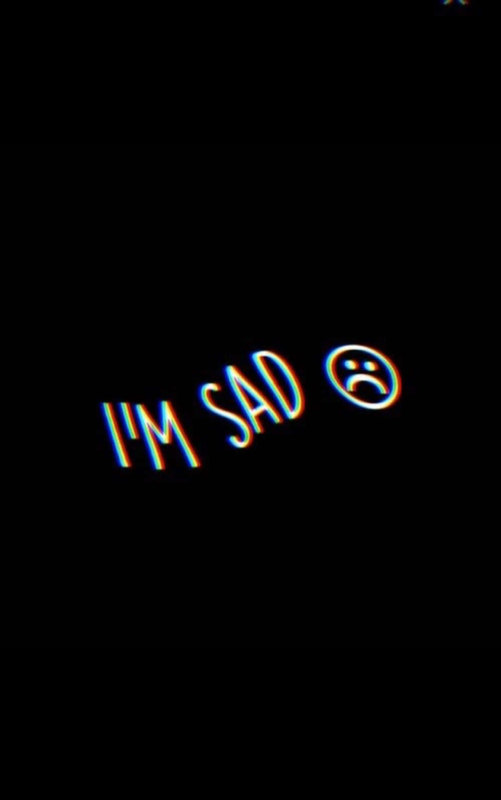 霓虹文字寫著「I'M SAD」，附有悲傷表情符號，背景為黑色。