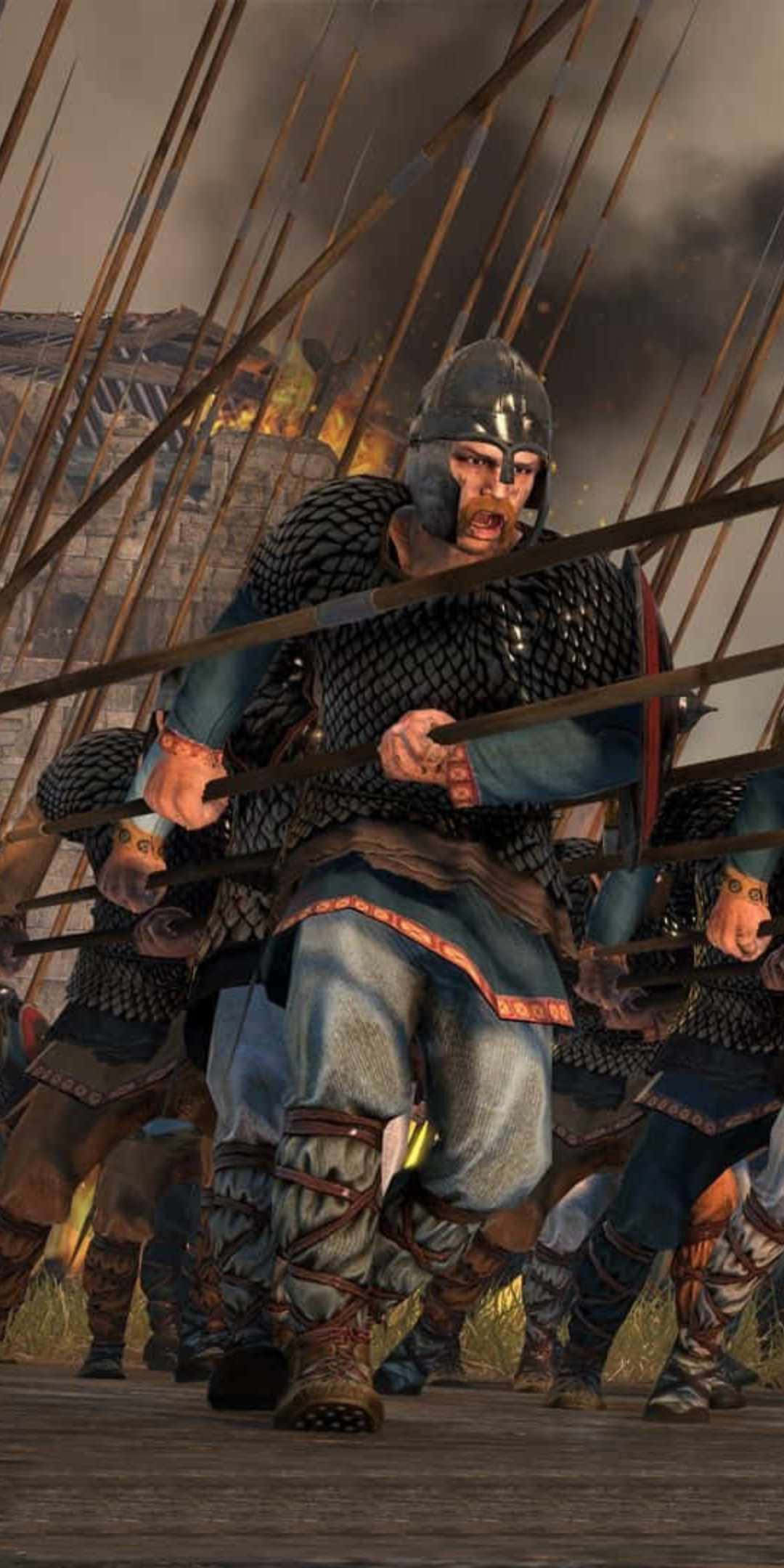 像素3《全面戰爭：阿提拉》東哥特士兵背景 壁紙 — 一名身穿鎖子甲和頭盔的兇猛中世紀戰士，在背景有燃燒建築物和長矛的混亂戰場上向前衝鋒。