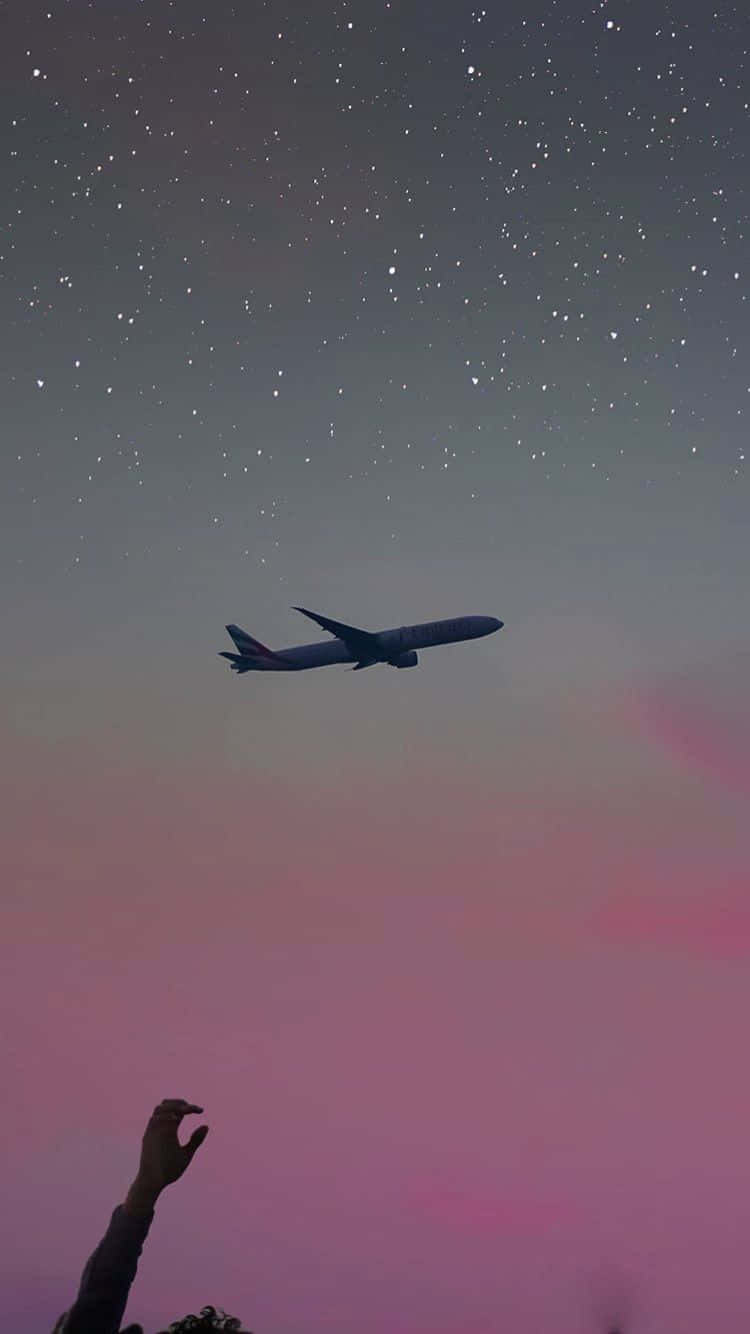 一隻手向上伸向一架飛行的飛機，背景是佈滿星星的粉紅色和紫色天空。