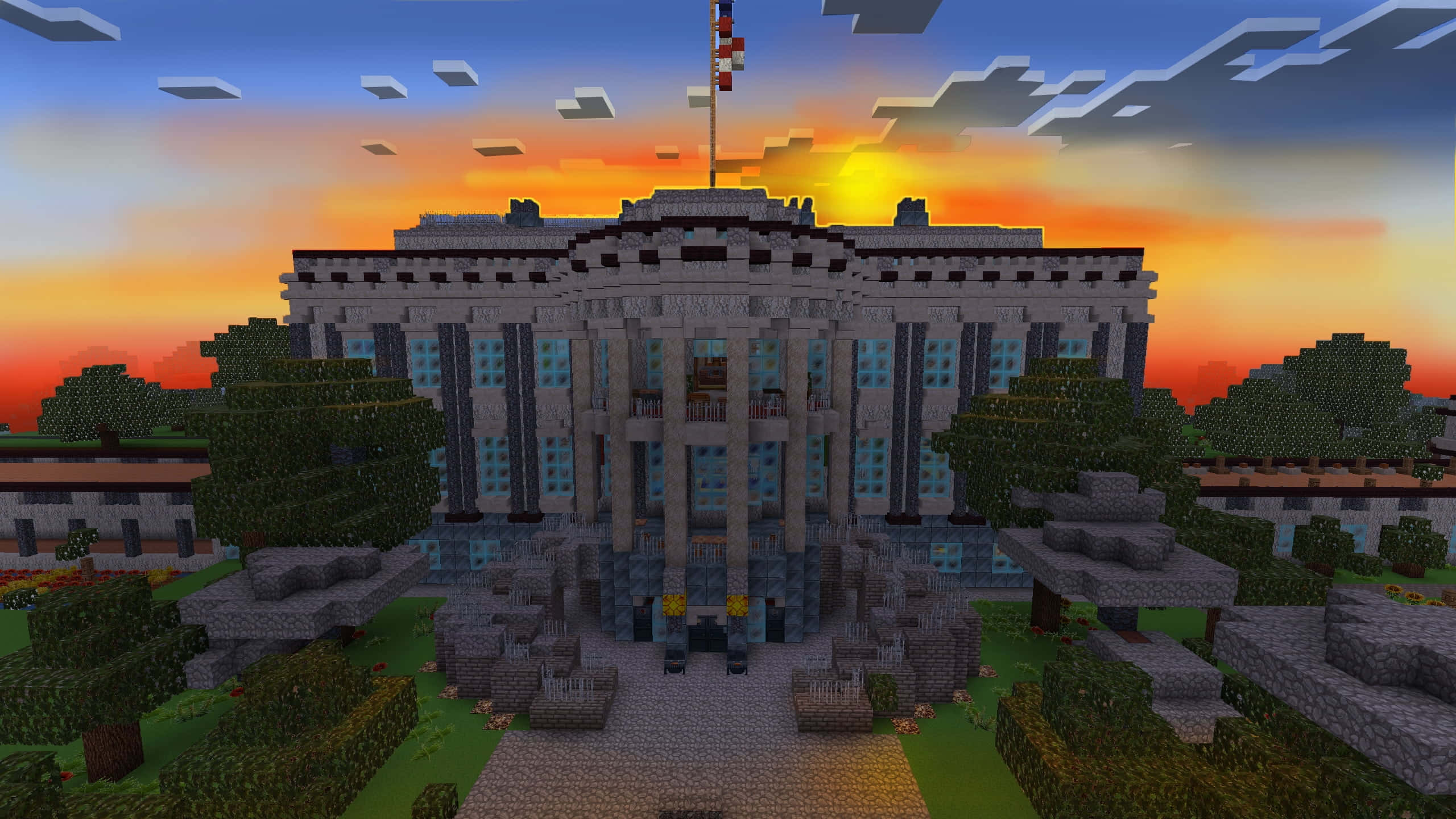 Minecraft Adventure 桌布 壁紙 — 像素化的Minecraft白宮複製品在日落時分雄偉矗立，周圍是鮮豔的橙色天空和方塊狀樹木。