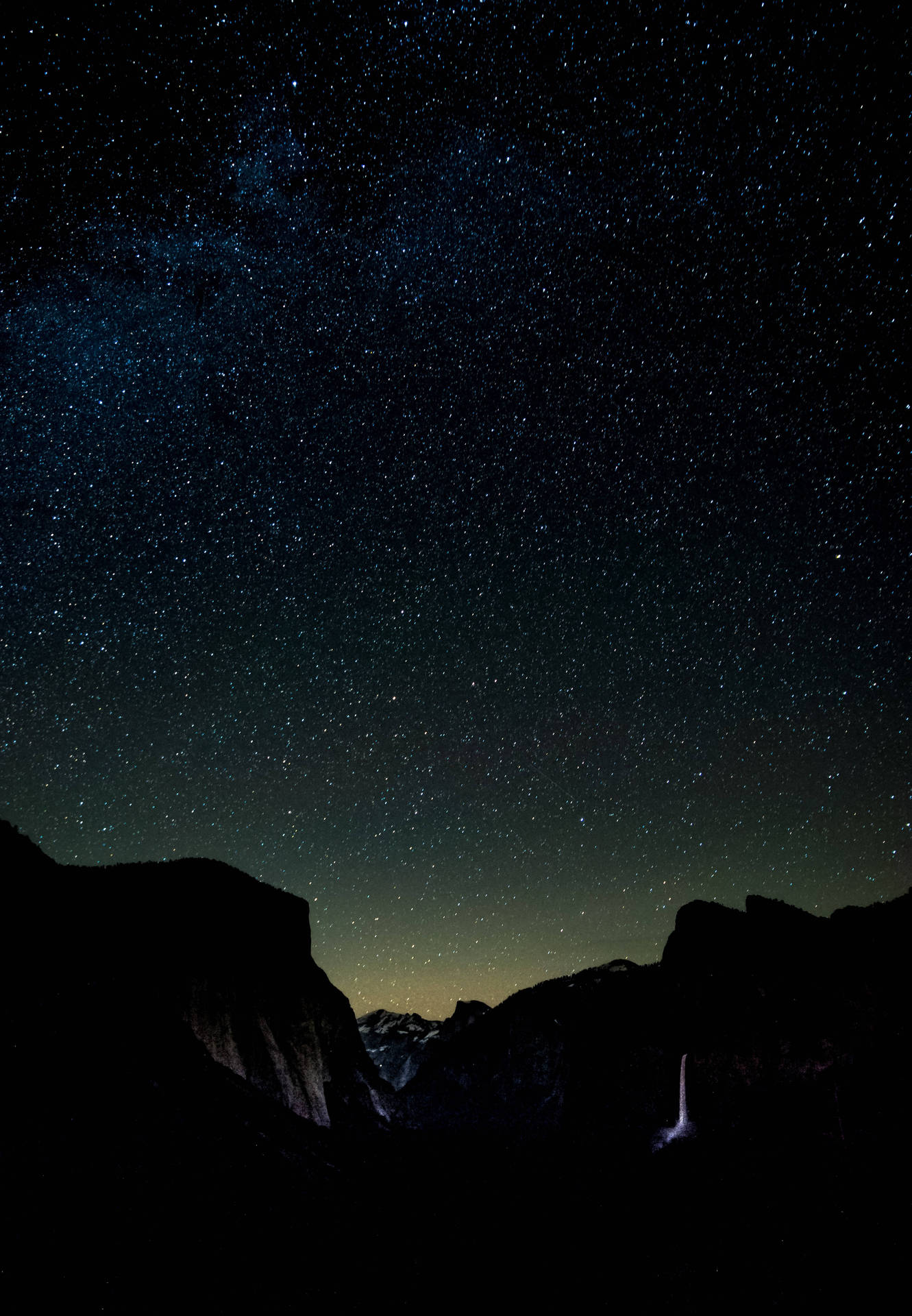 黑暗的山巒在繁星點點、帶有銀河的夜空下襯托著發光的瀑布。