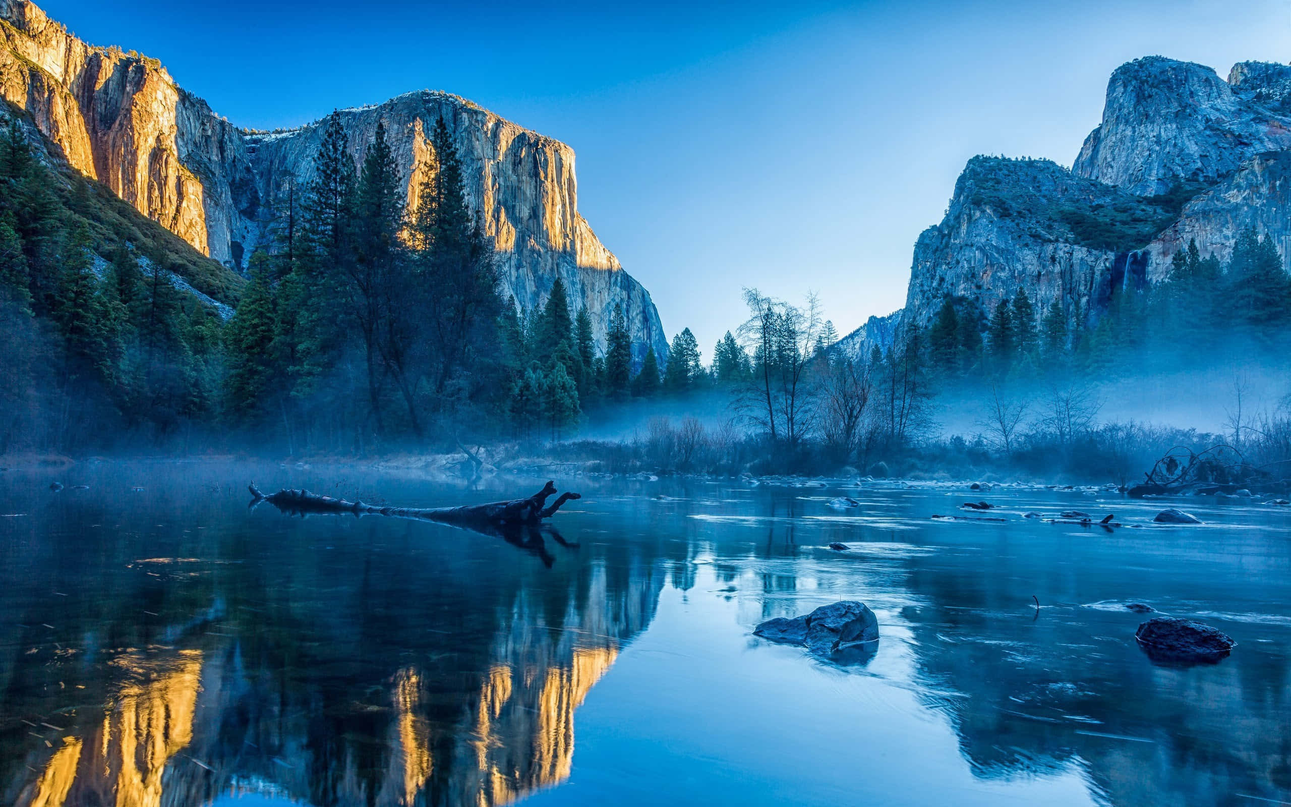 High Sierra 桌布 壁紙 — 優勝美地山谷霧氣瀰漫的黎明，金色懸崖倒映在平靜的藍色河流中，四周環繞著松樹。