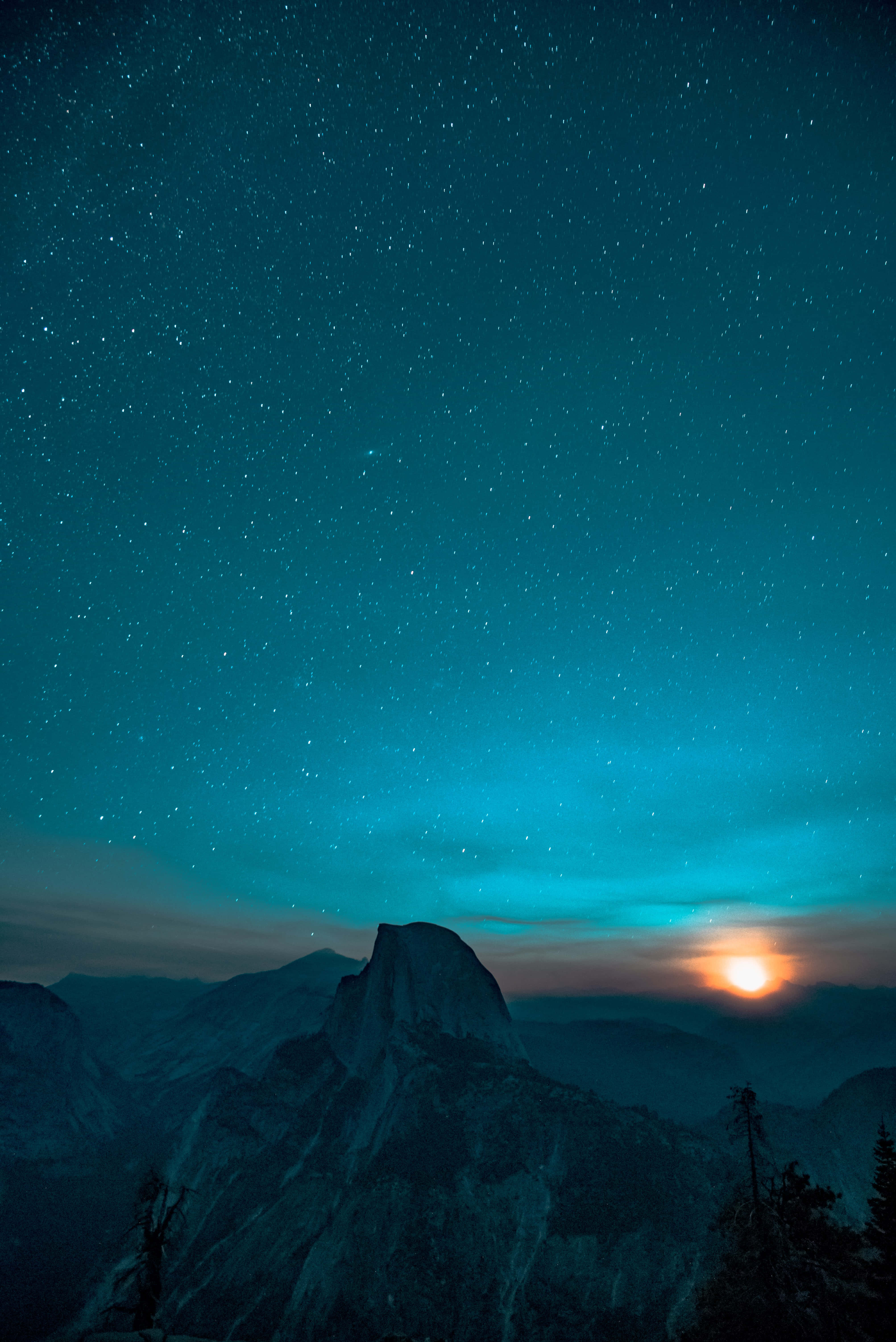 優美約塞米蒂山夜空繁星iPhone背景 壁紙 — 雄偉的山峰在繁星點點的暮色天空中形成剪影，一輪發光的太陽在地平線上落下。