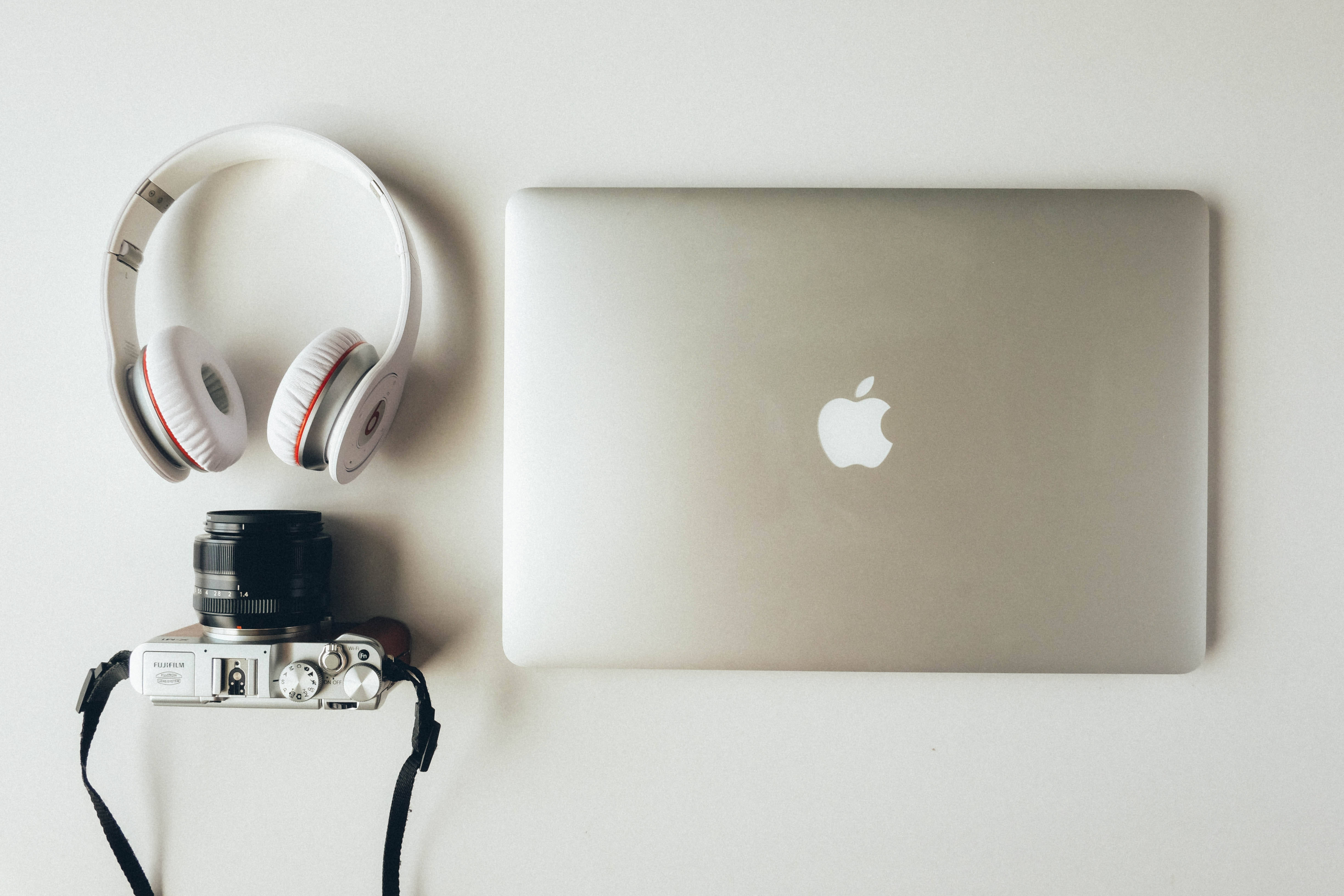 優雅 Apple Mac 設計 壁紙 — 一部時尚的銀色手提電腦帶有Apple標誌，旁邊放著白色耳機和銀色相機，在簡約的白色表面上。
