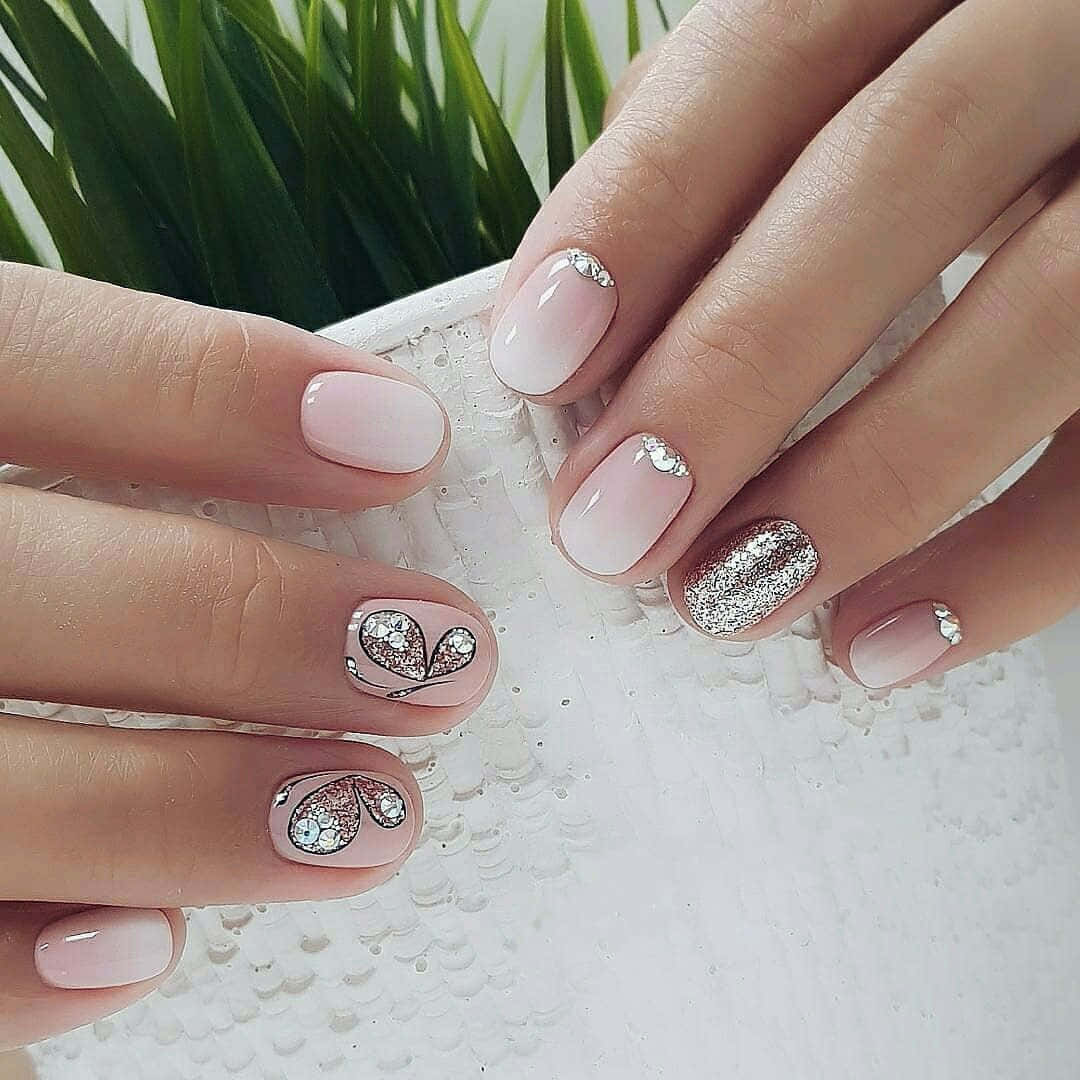 Spring Nails 桌布 壁紙 — 優雅嘅手，帶有柔和粉紅色漸變指甲，飾有閃粉心形同銀色水鑽，放喺綠色植物旁邊。