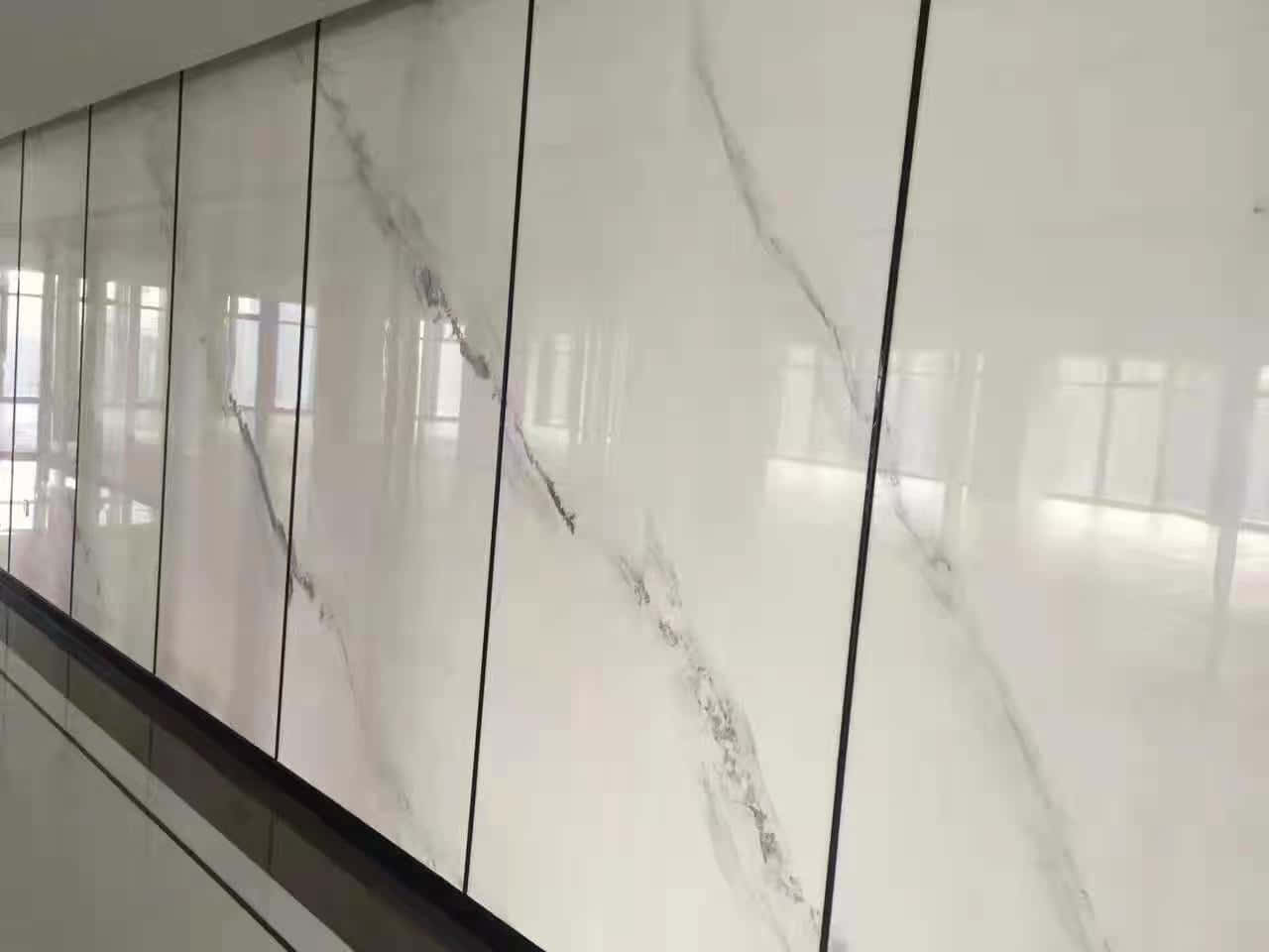 現代走廊中帶有灰色紋理和黑色接縫的光面白色大理石牆板。