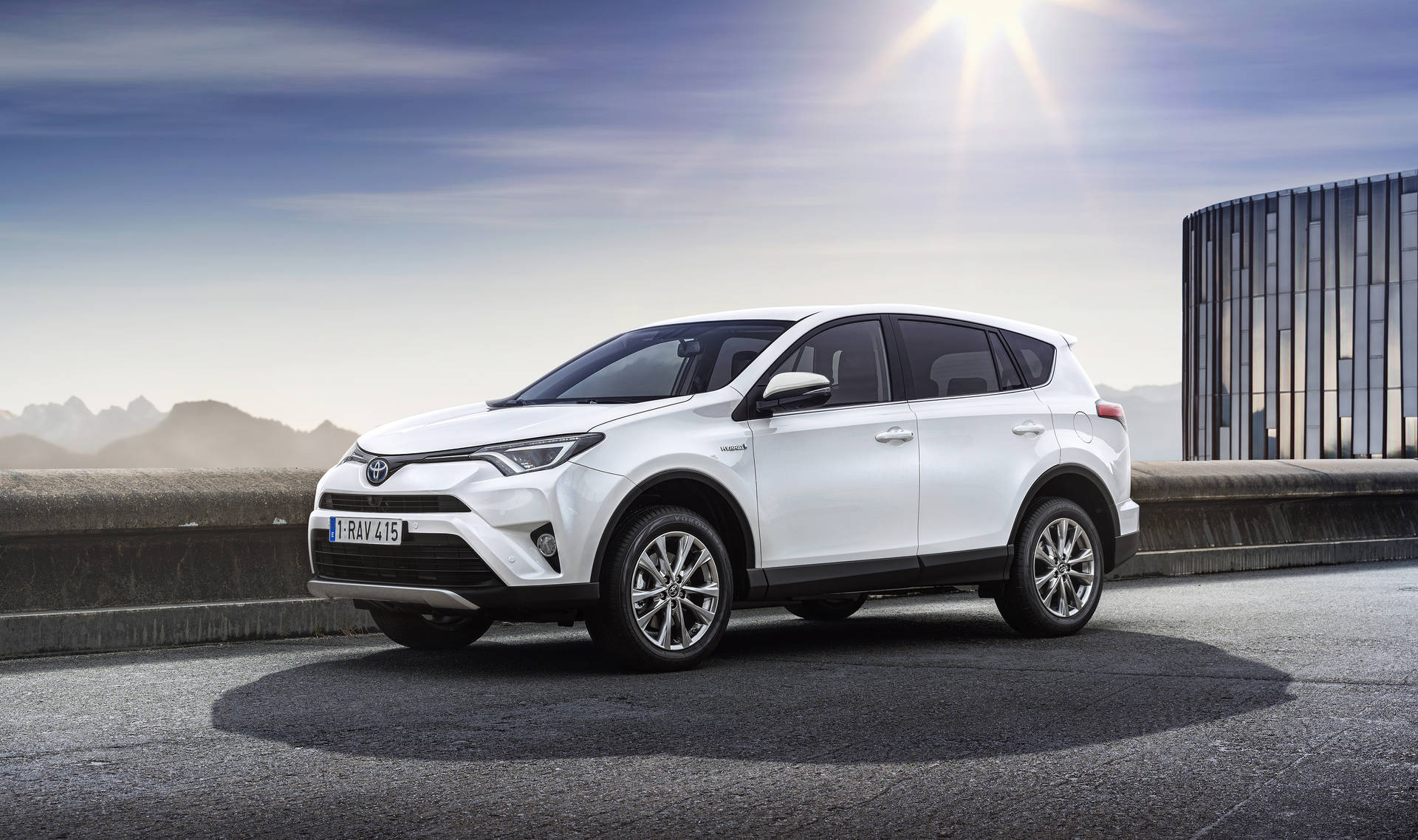 白色豐田RAV4 SUV在橋上，背景有山脈和現代建築。