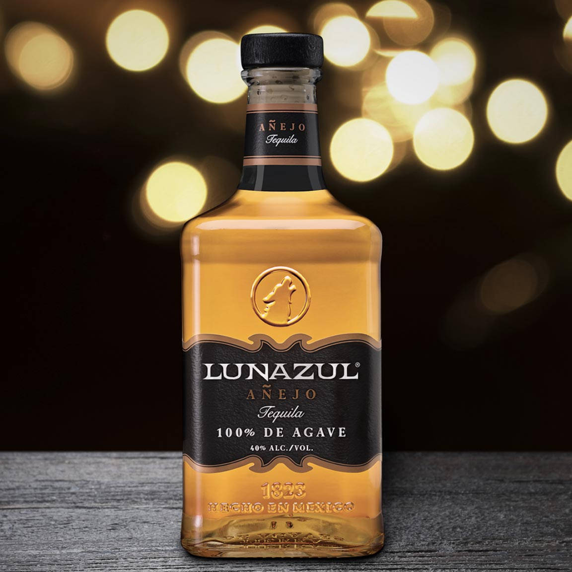 優雅的 Lunazul Anejo 蒂克酒瓶 壁紙 — 一瓶Lunazul Añejo龍舌蘭酒在木質表面上閃耀，背景是溫暖的金色散景燈光。