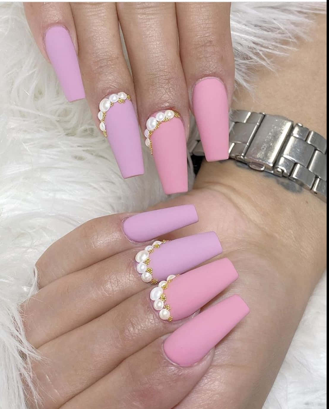 Pink Nails 桌布 壁紙 — 優雅的手，帶有啞光粉紅色棺材形指甲，飾有珍珠和金色點綴，放在蓬鬆的白色表面上。