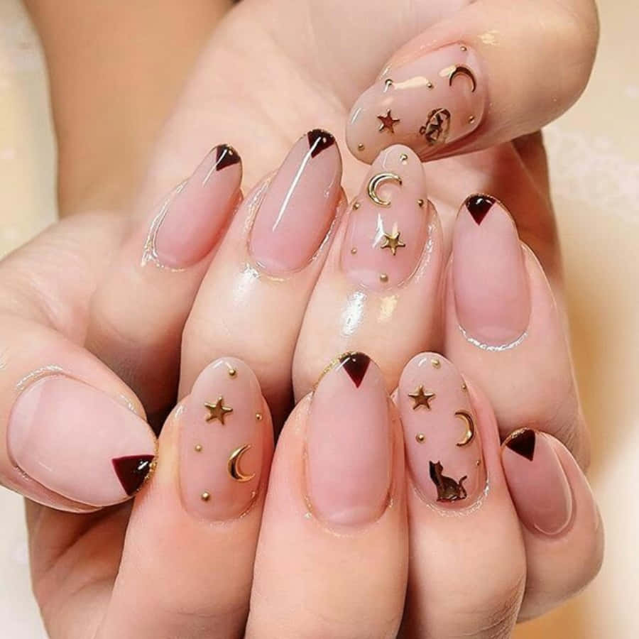 Pink Nail Art 桌布 壁紙 — 優雅的手，裸色指甲上飾有金色星星、月亮和貓剪影，背景為柔和米色。