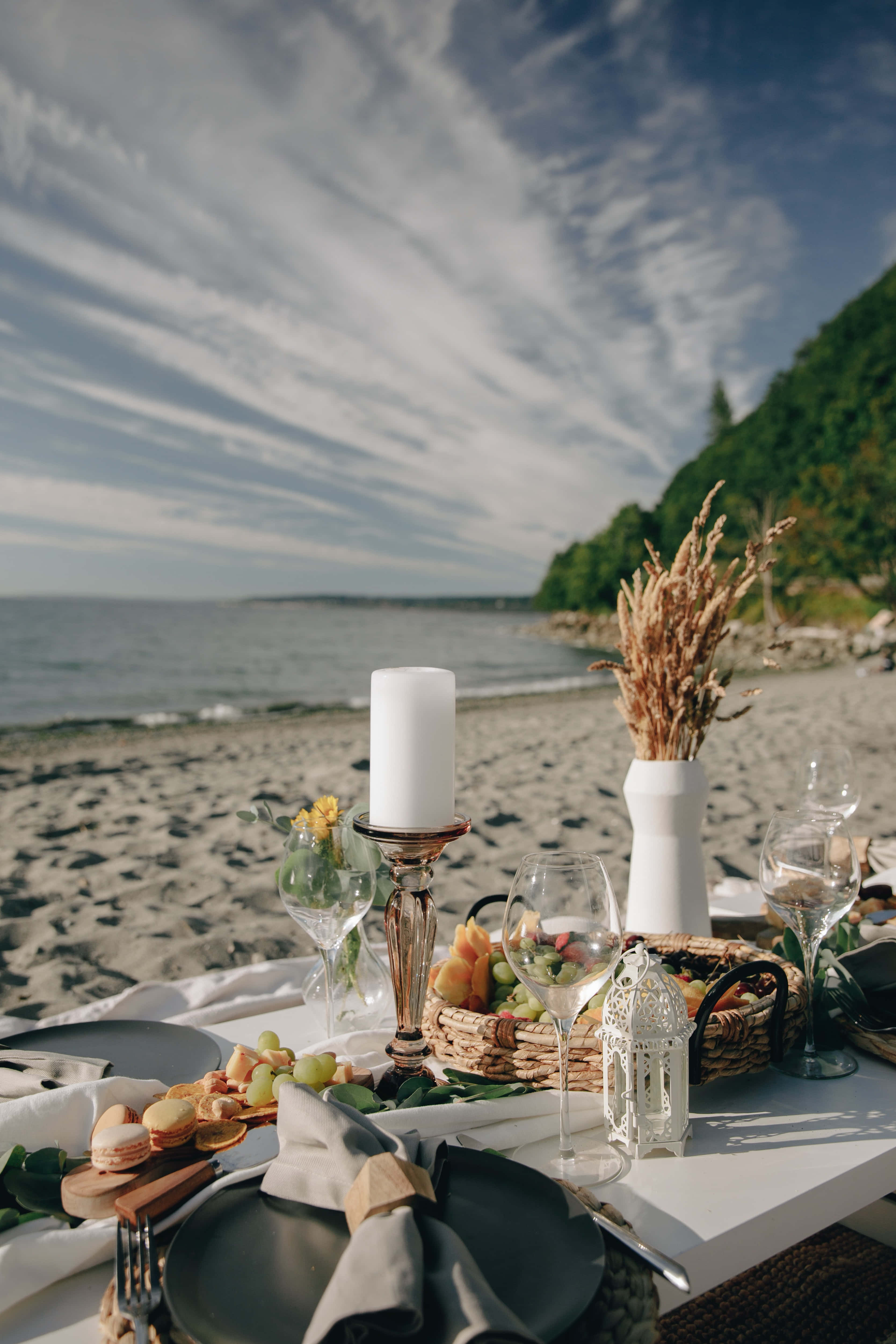 Beach Picnic 桌布 壁紙 — 優雅的海邊餐桌，擺放深色碟子、玻璃器皿和乾草，在明亮的天空下。