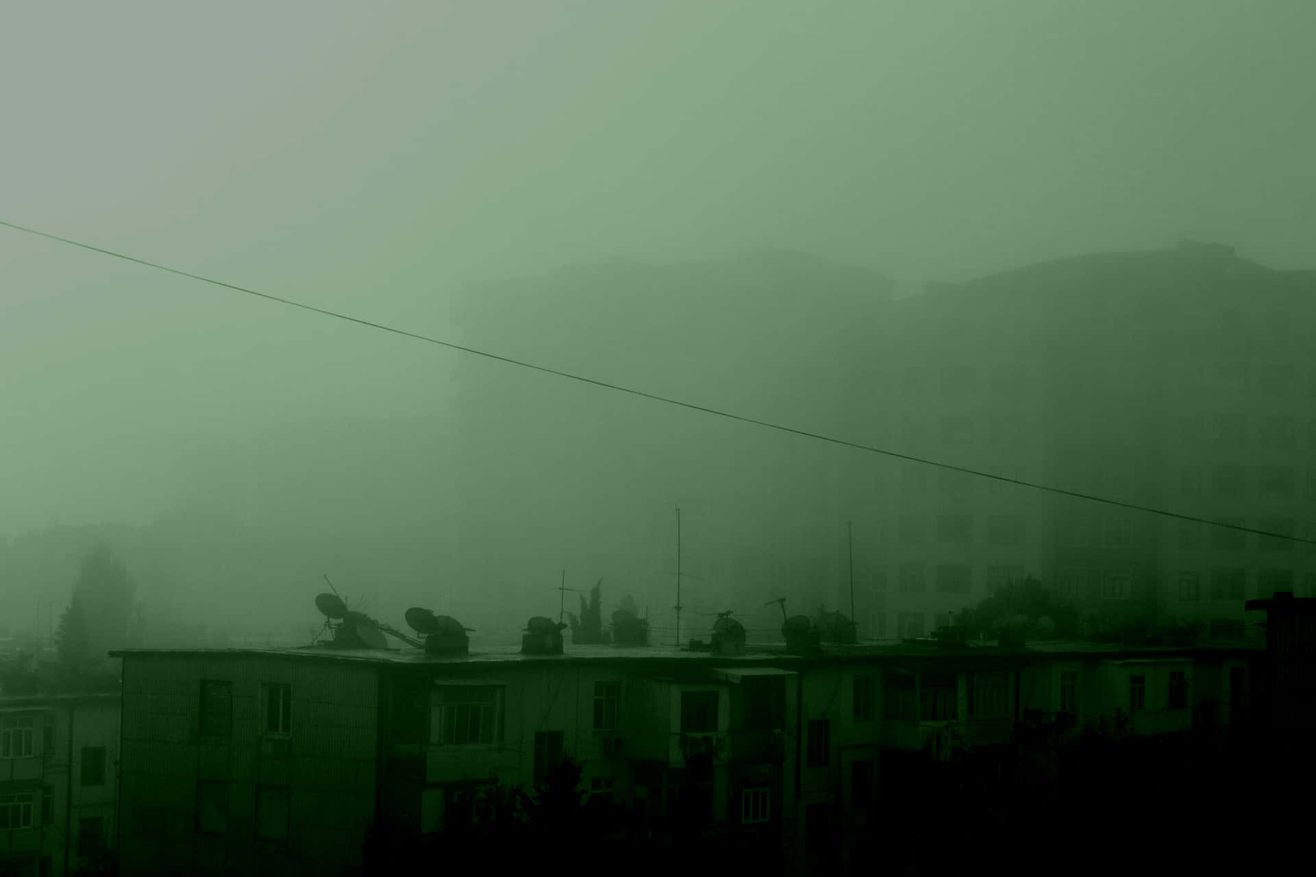 在綠色薄霧下的霧氣城市建築，一條電線劃過天空。