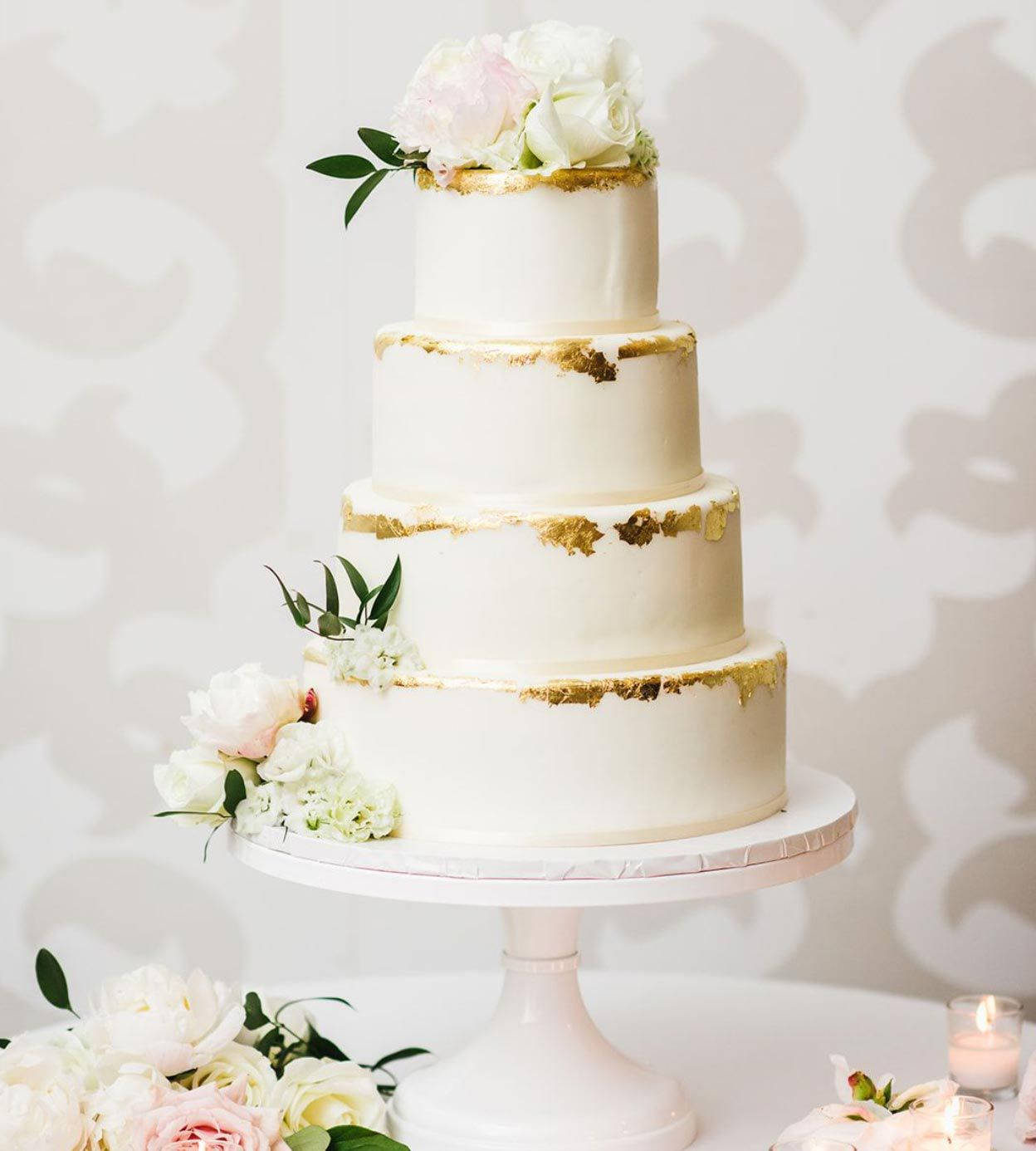 優雅的白金邊婚禮蛋糕 壁紙 — 一個四層白色結婚蛋糕，飾有金箔和新鮮粉紅白玫瑰，優雅地放在白色支架上。