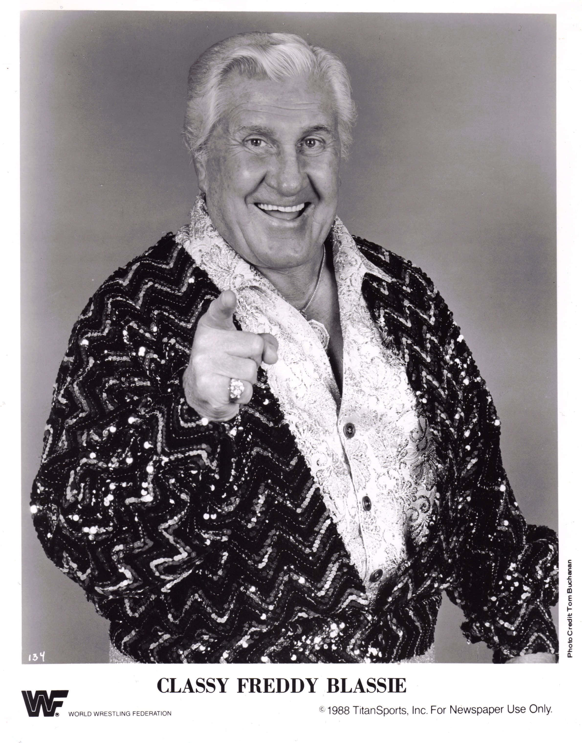 優雅的美國摔角手弗雷迪·布拉斯比 壁紙 — Classy Freddy Blassie 燦爛地微笑，並穿著閃亮亮片外套直接指向觀眾。