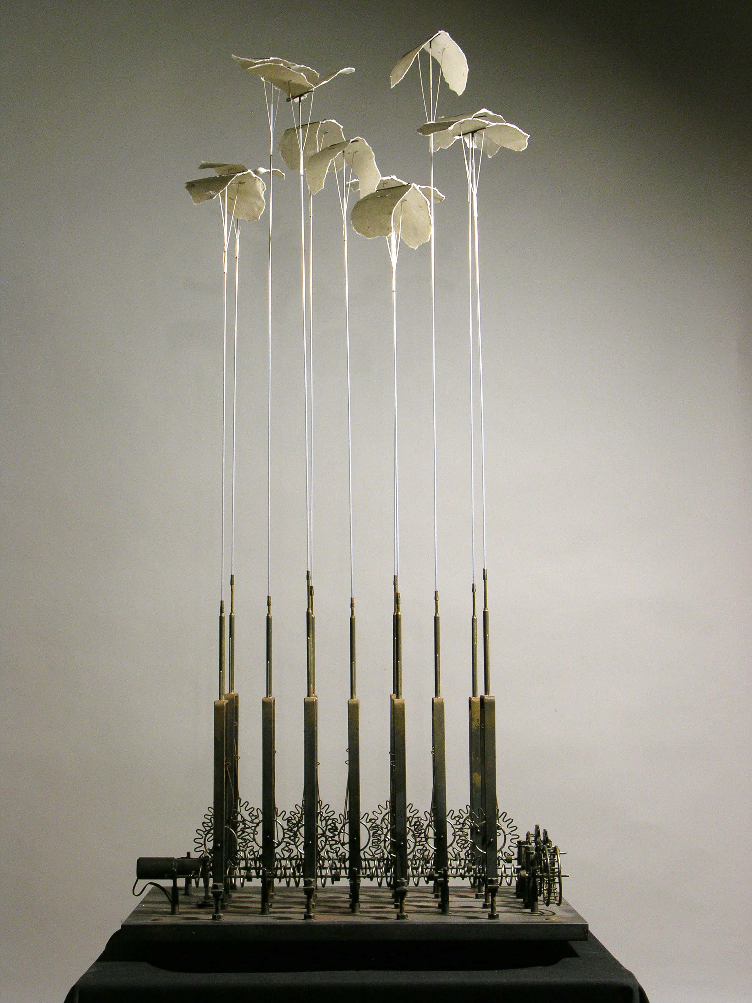 Kinetic Art 桌布 壁紙 — 優雅的金屬雕塑，精緻的白色花瓣狀形態懸掛在纖細的桿子上，襯以柔和的灰色背景。