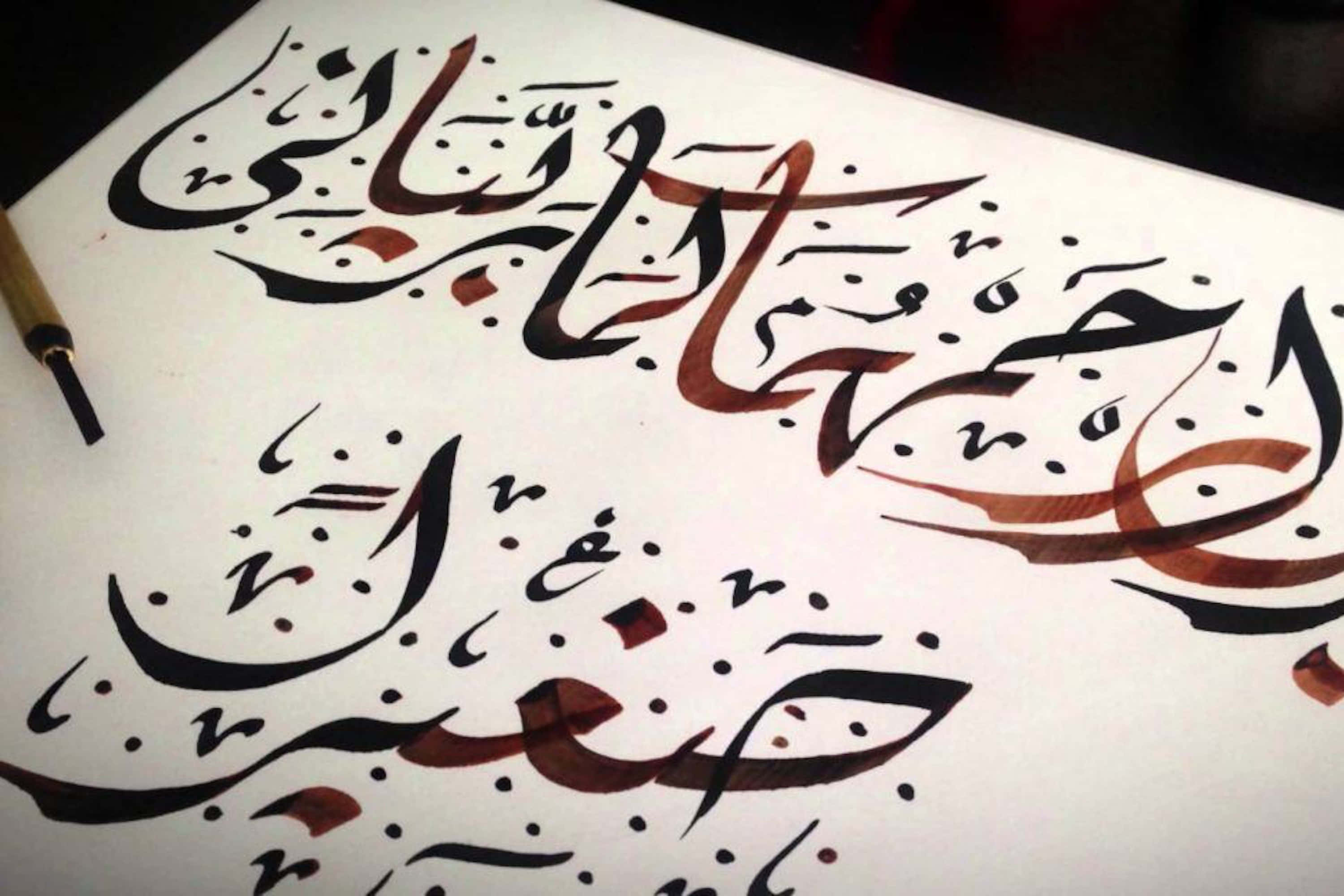 arabic 桌布 壁紙 — 優雅的阿拉伯書法以黑色和棕色墨水在白色紙張上流動，旁邊放著一支毛筆。