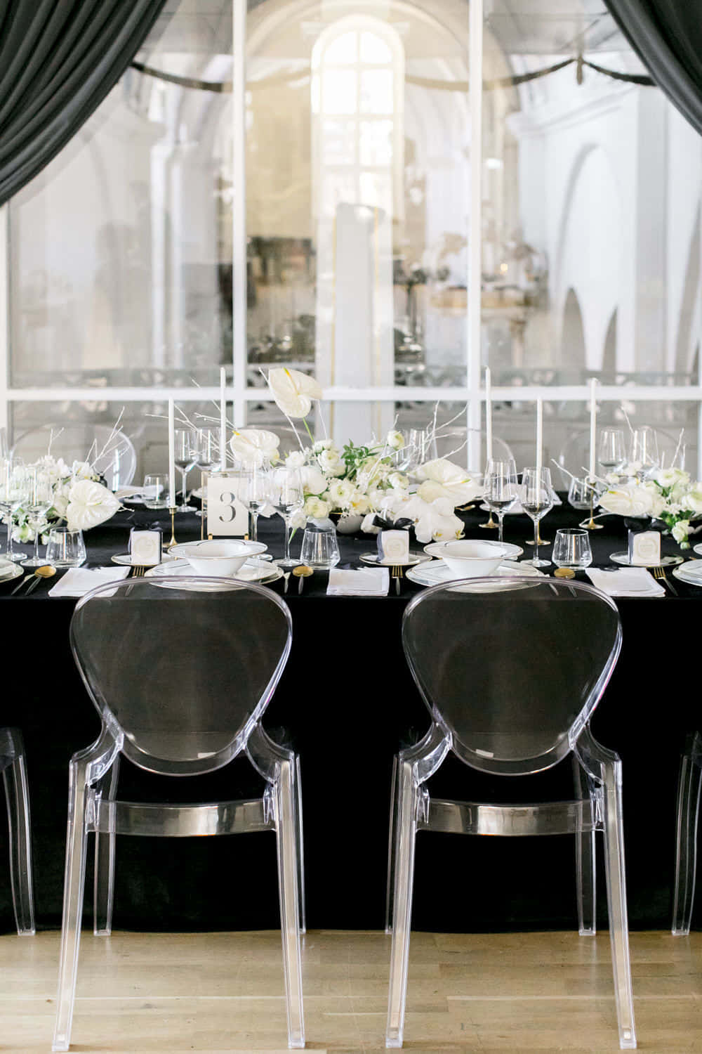 Black And White Wedding 桌布 壁紙 — 優雅的黑色餐桌套裝，配有白色花卉和玻璃椅，位於拱形窗戶和垂簾之下。