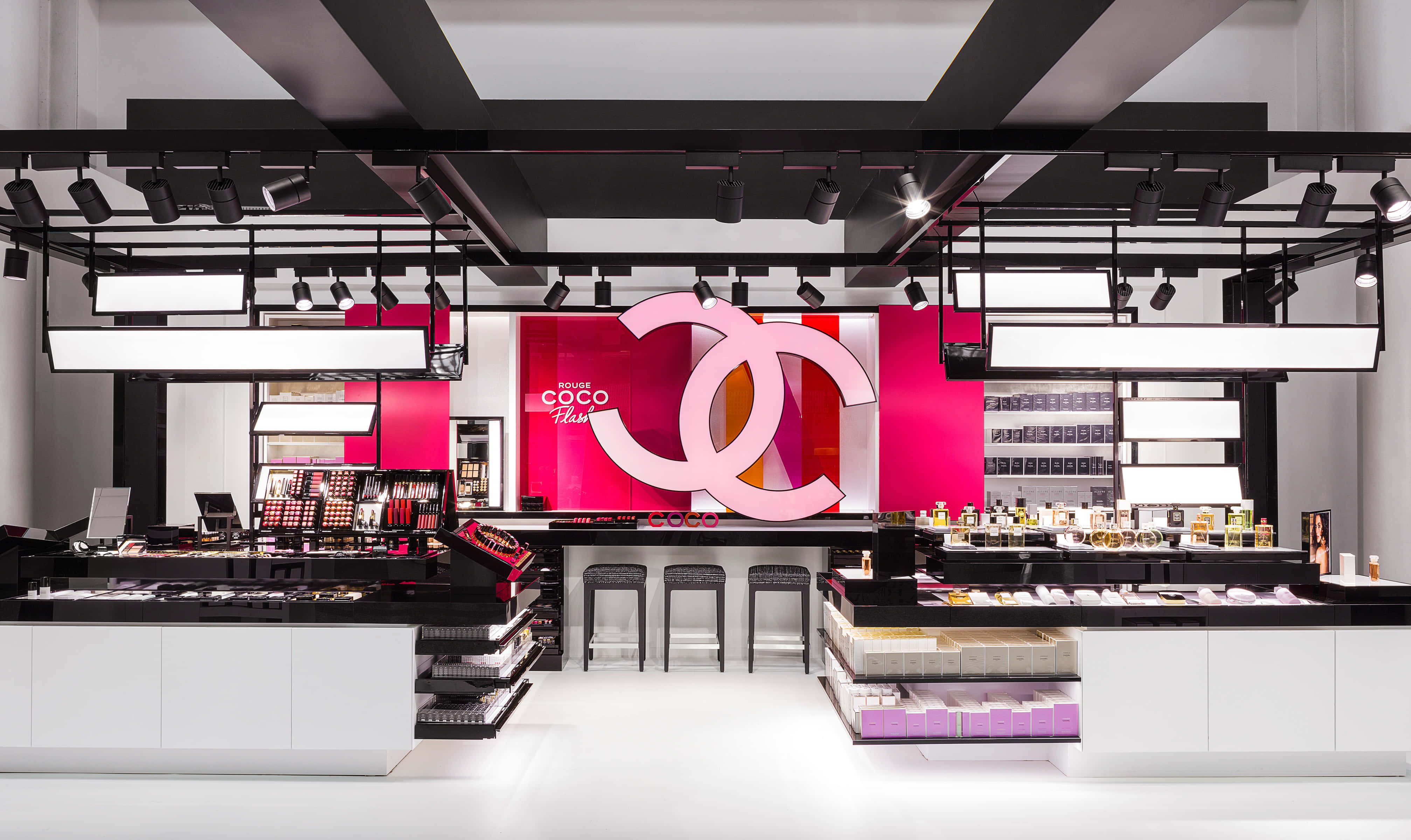 優雅與奢華的典範：香奈兒 壁紙 — 時尚現代的 Chanel 化妝品精品店，採用大膽的粉紅色品牌、黑色裝置和明亮的聚光燈照亮產品展示。