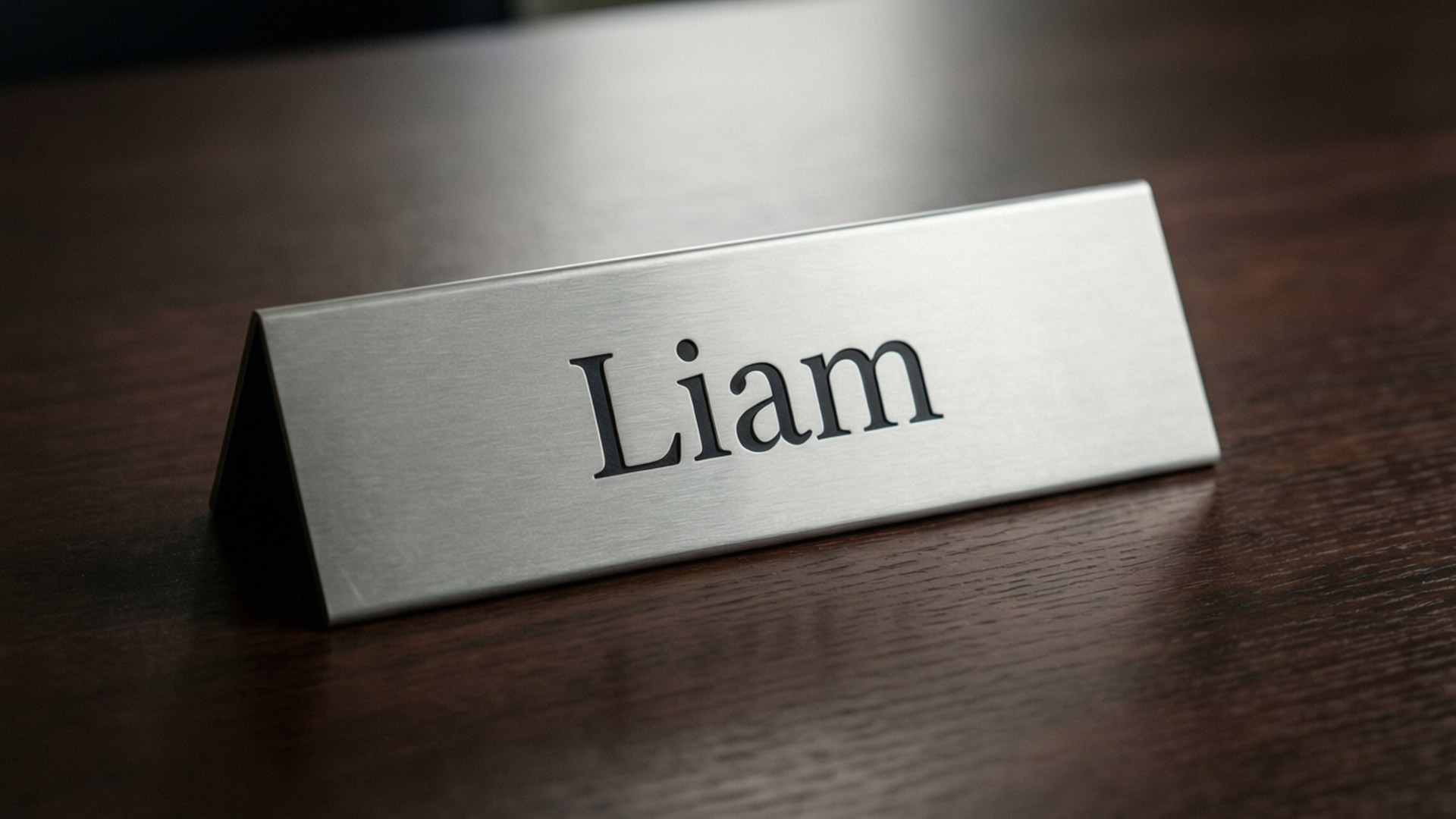 銀色名牌，上面刻有 Liam 的名字，置於深色木質表面。