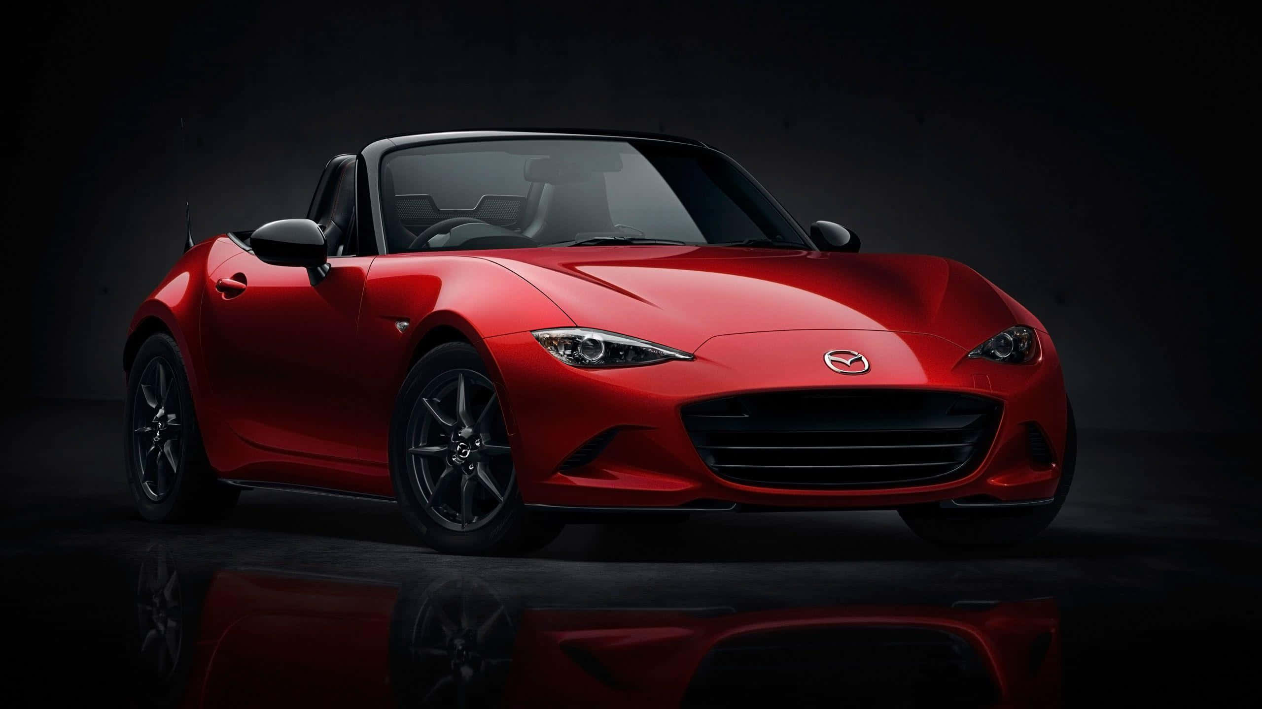 優雅馬自達MX-5 Miata運動跑車 壁紙 — 一輛光澤的紅色萬事得MX-5 Miata開篷車在深色反光地板上於攝影棚燈光下閃耀。
