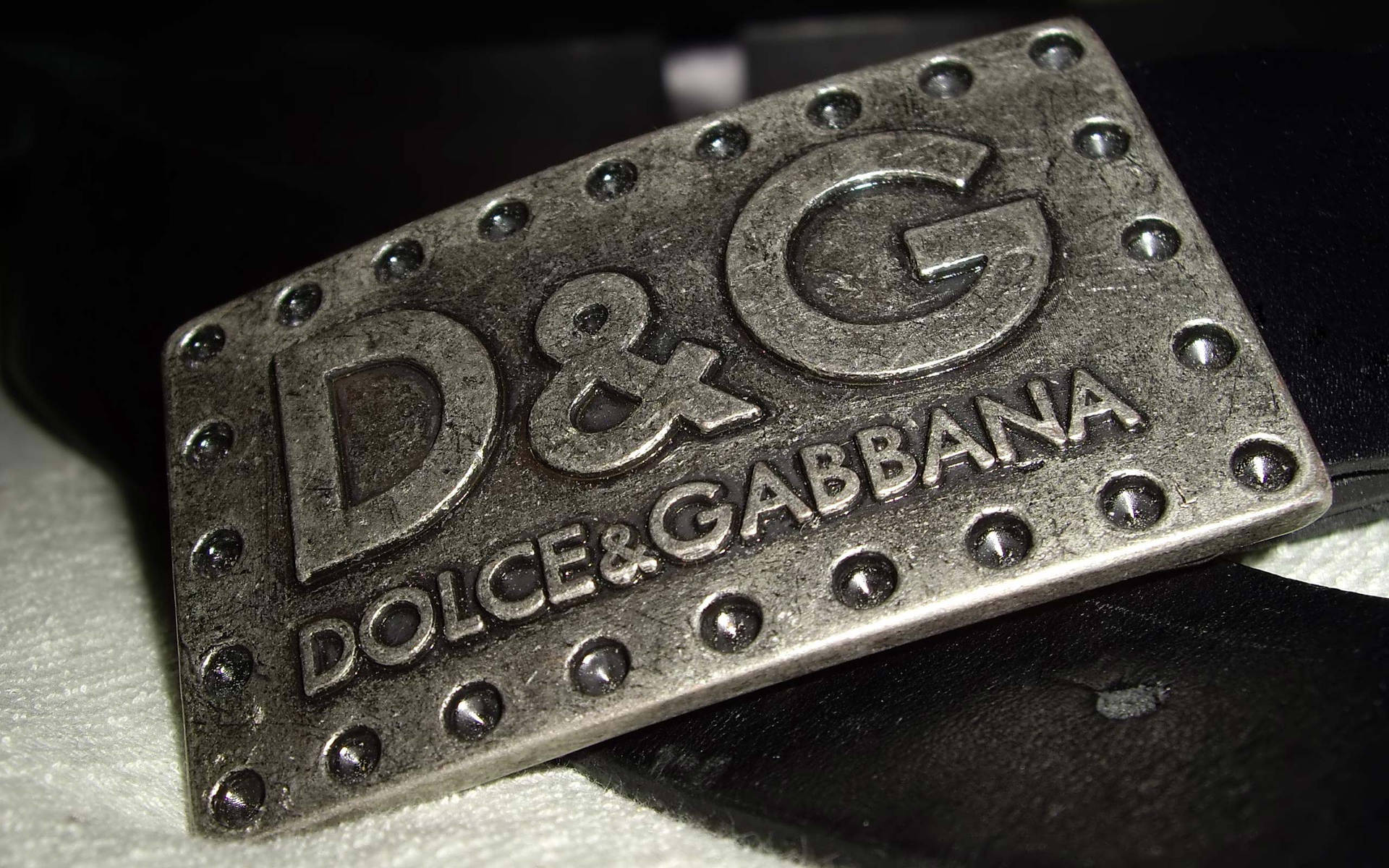 帶有鉚釘的銀色 Dolce & Gabbana 皮帶扣，放置在黑色皮革和白色布料上。