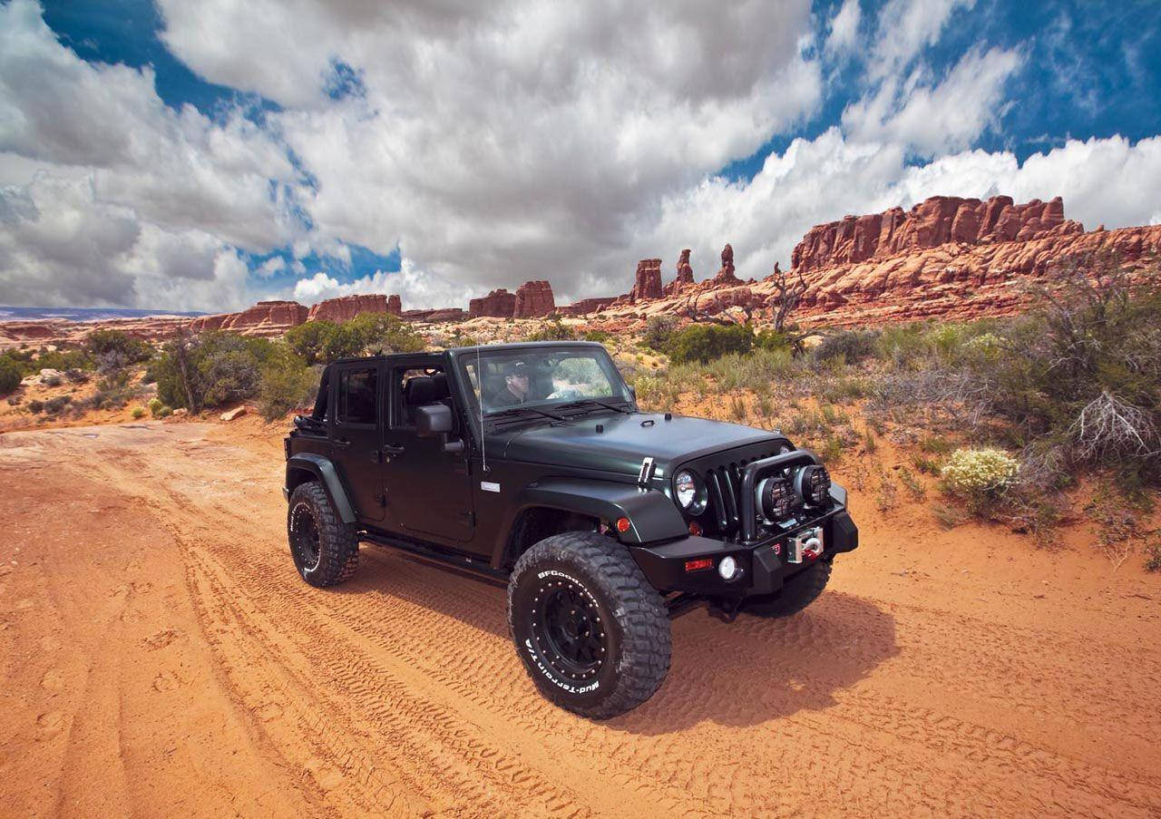 黑色Jeep Wrangler在紅色岩石沙漠景觀的泥路上行駛。