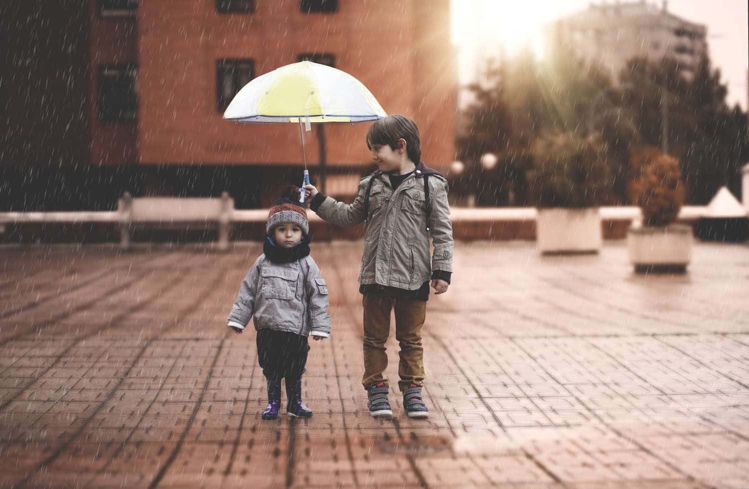 兩個孩子在磚砌廣場上撐著雨傘在雨中行走。