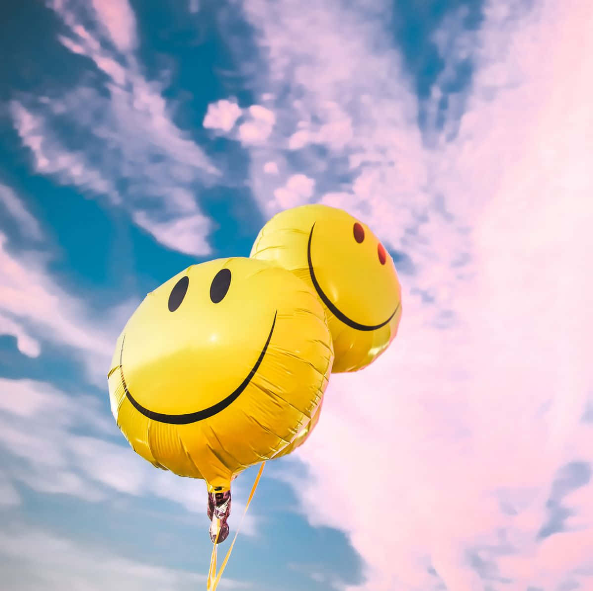 兩個黃色笑臉氣球漂浮在粉紅色和藍色的天空中。