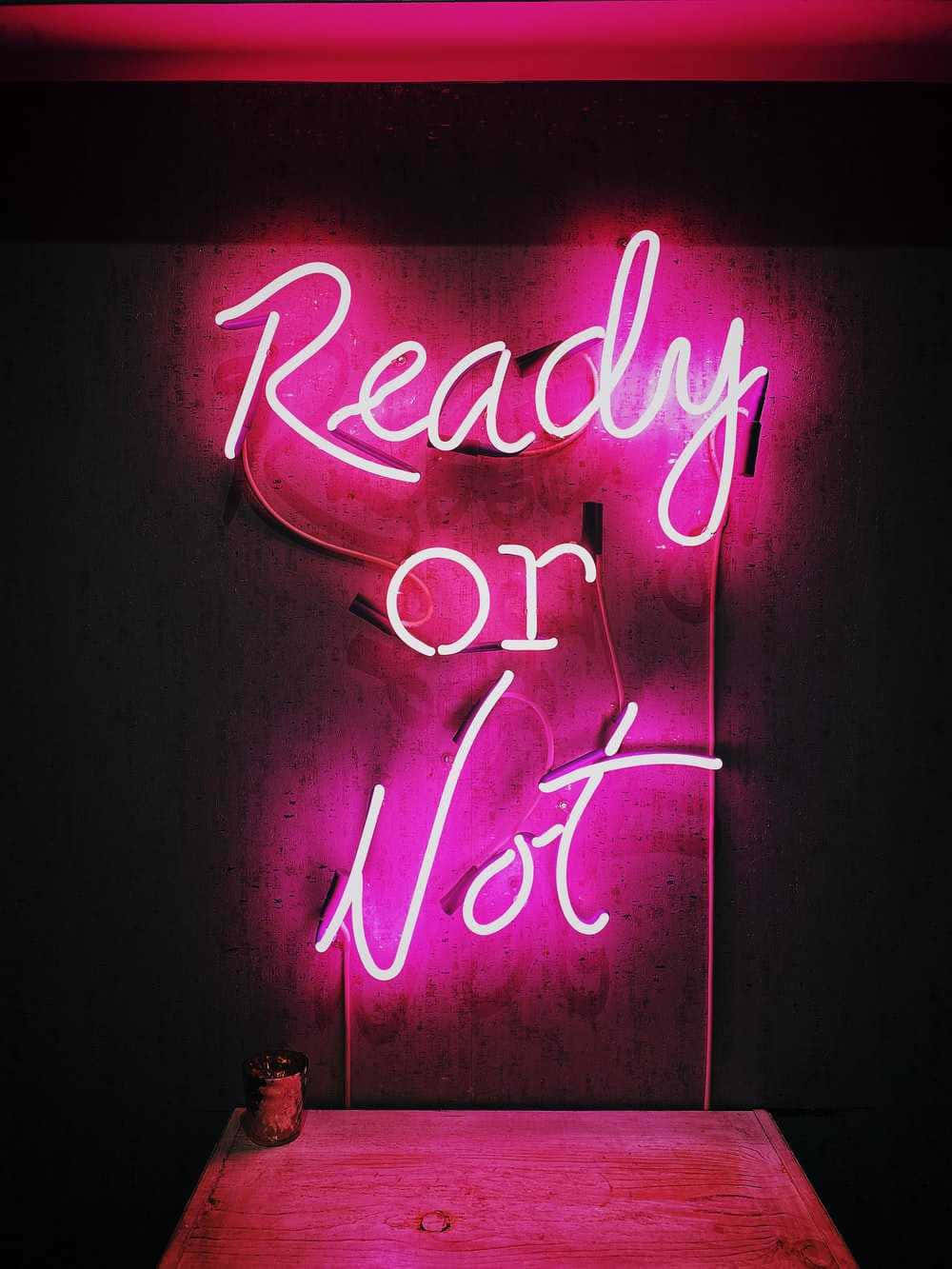 深色牆壁上、木桌上方，一個寫着「Ready or Not」的粉紅色霓虹燈牌。