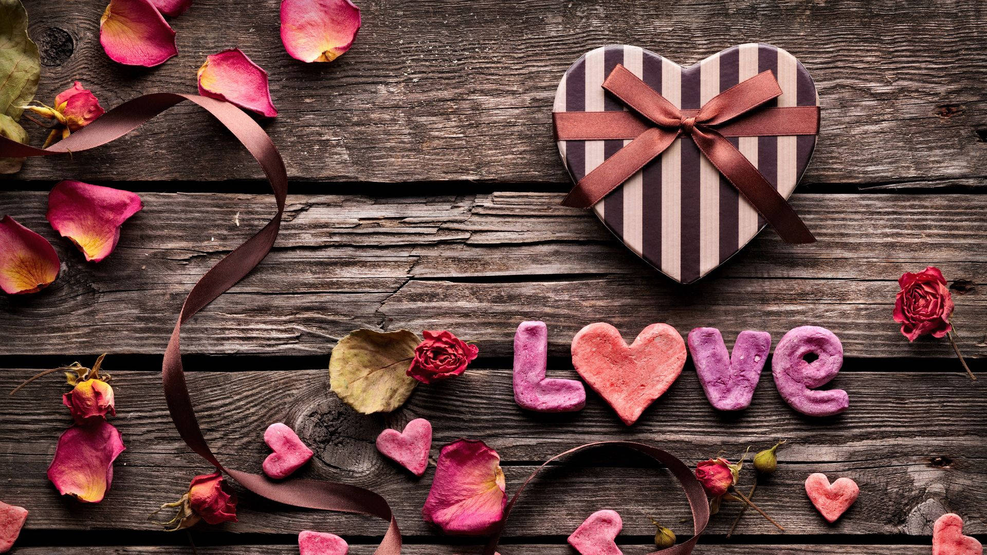 心形禮物盒和粉紅色糖字母拼出 love 在木桌上，伴有玫瑰花瓣。