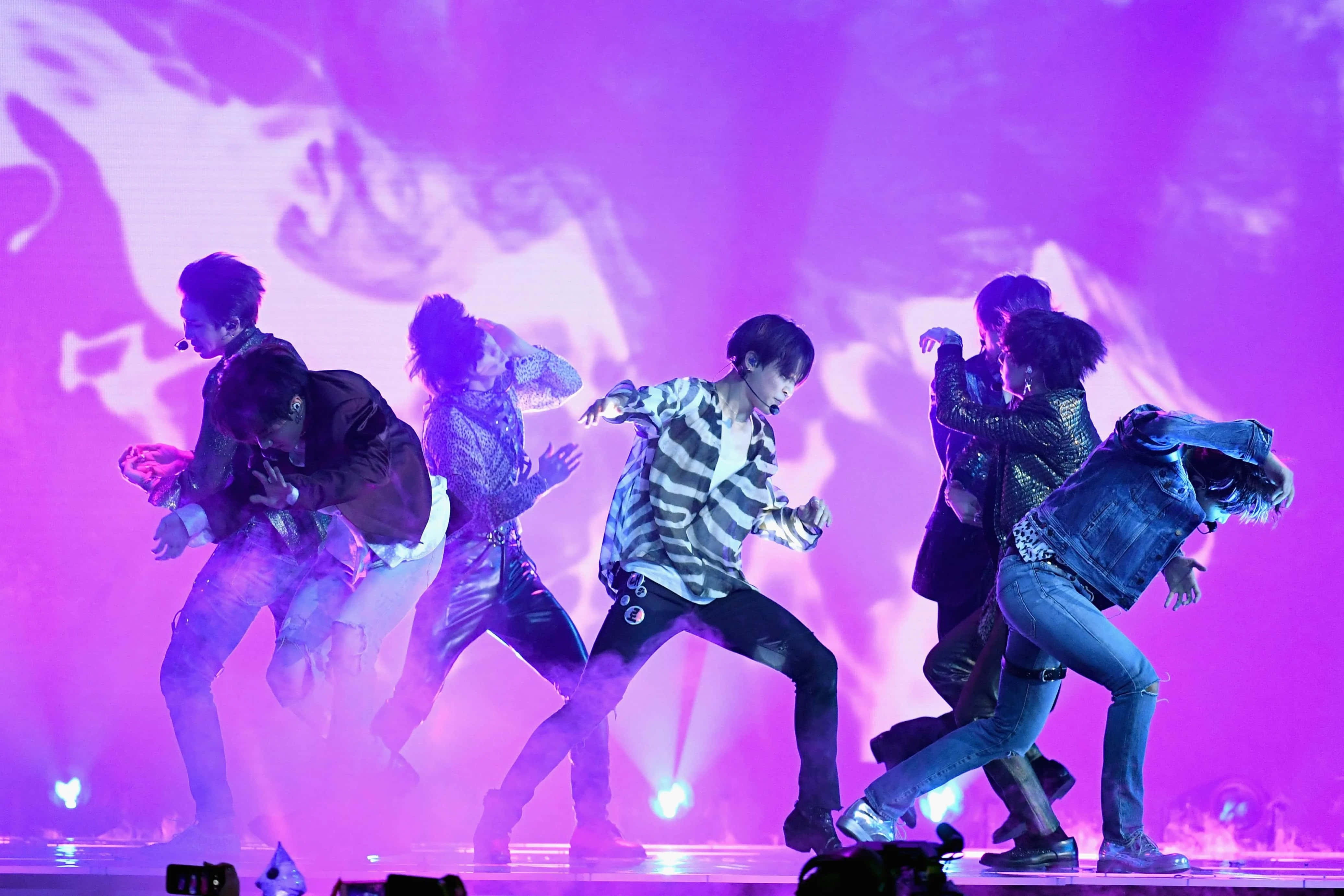 Bts Stage 桌布 壁紙 — 充滿活力的K-pop表演者在鮮豔的紫色舞台燈光下擺出同步的舞蹈姿勢。