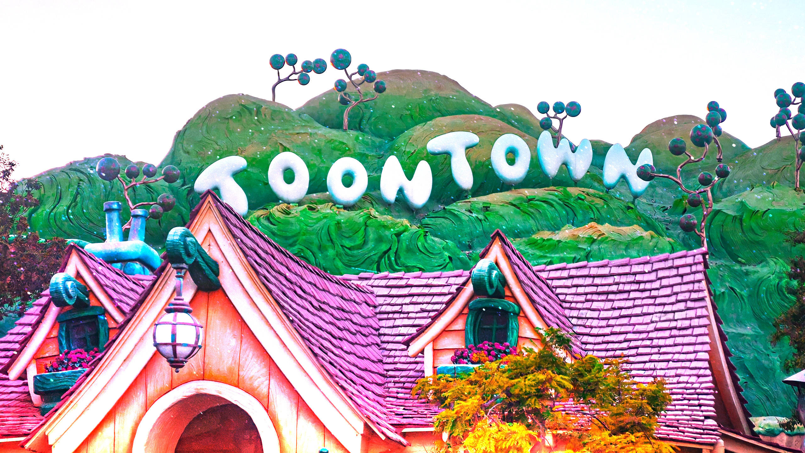 Minnie Mouse 桌布 壁紙 — 充滿活力的卡通風格Toontown標誌，位於紫色屋頂和綠色山丘上奇幻房屋之上，在明亮的天空下。