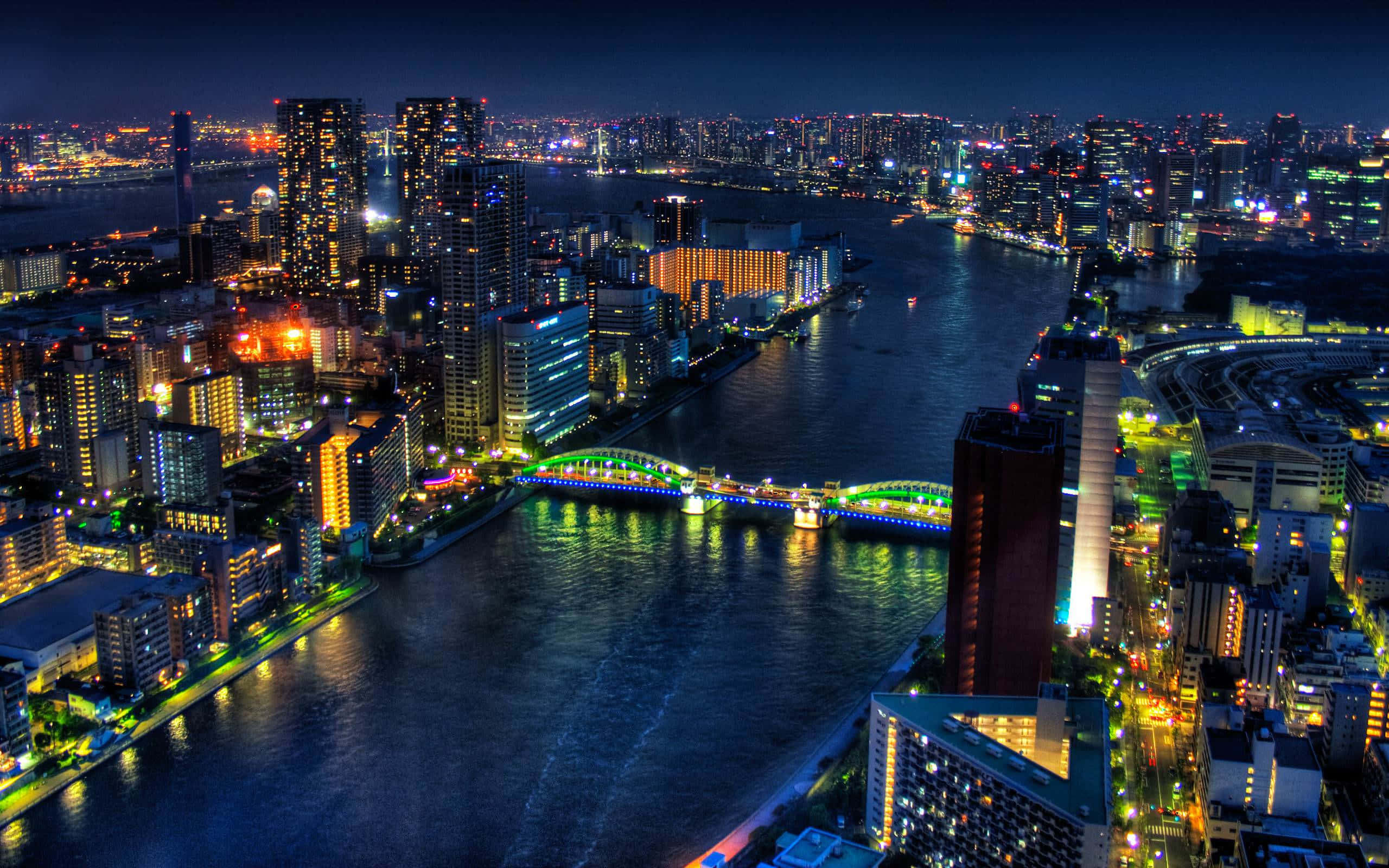 Cityscape 桌布 壁紙 — 充滿活力的城市景觀的空中夜景，有發光的摩天大樓和一座橫跨黑暗河流的彩色橋樑。