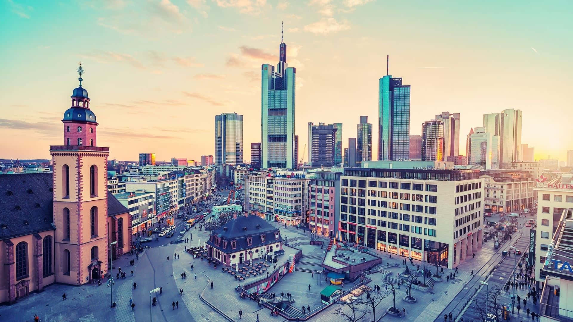 Germany 桌布 壁紙 — 充滿活力的夕陽以溫暖的色調沐浴著法蘭克福的天際線，歷史悠久的塔樓矗立在現代玻璃摩天大樓旁。
