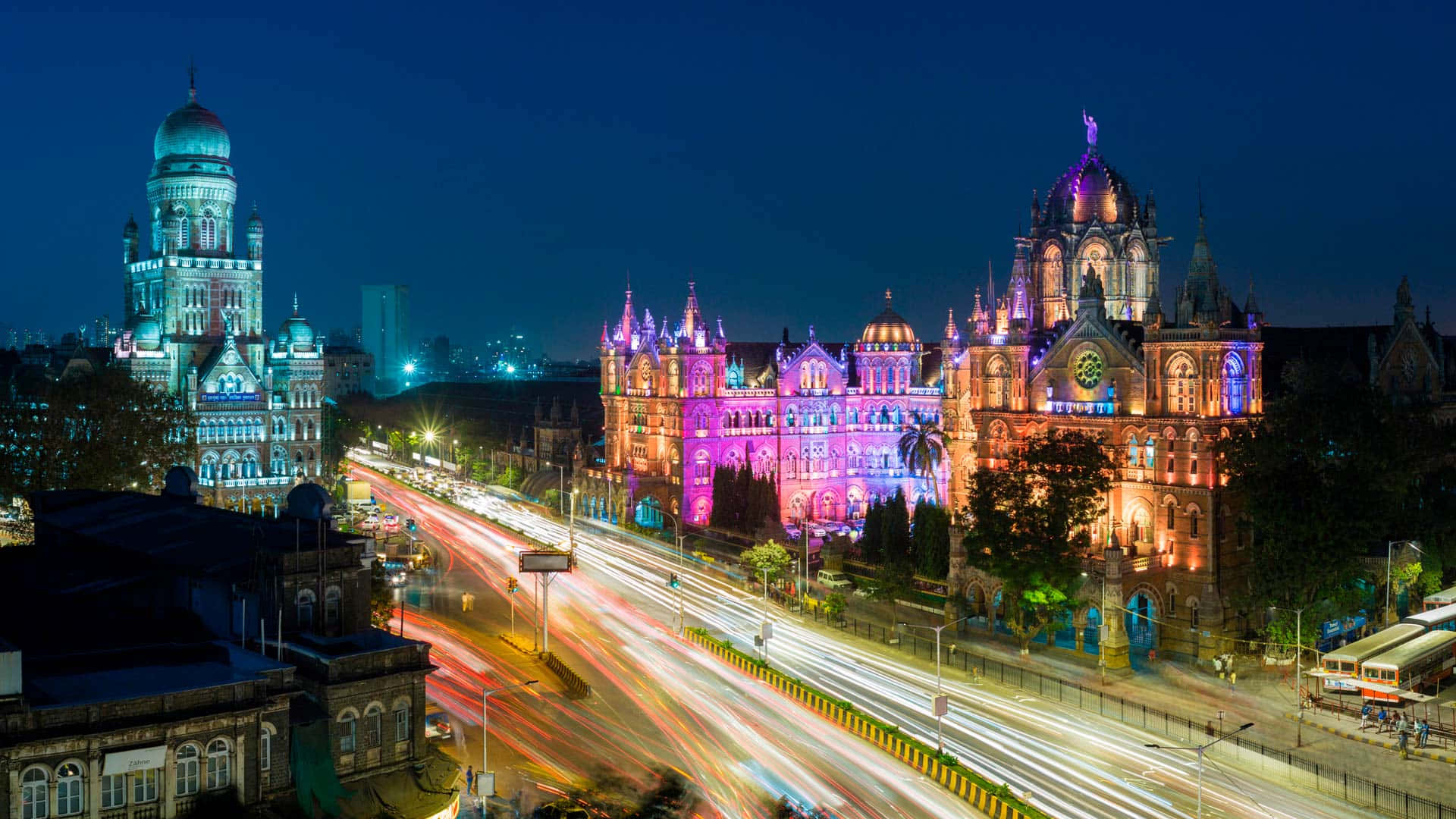Mumbai 桌布 壁紙 — 充滿活力的夜景，歷史建築在繽紛燈光下閃耀，下方的街道被車流燈光軌跡照亮。