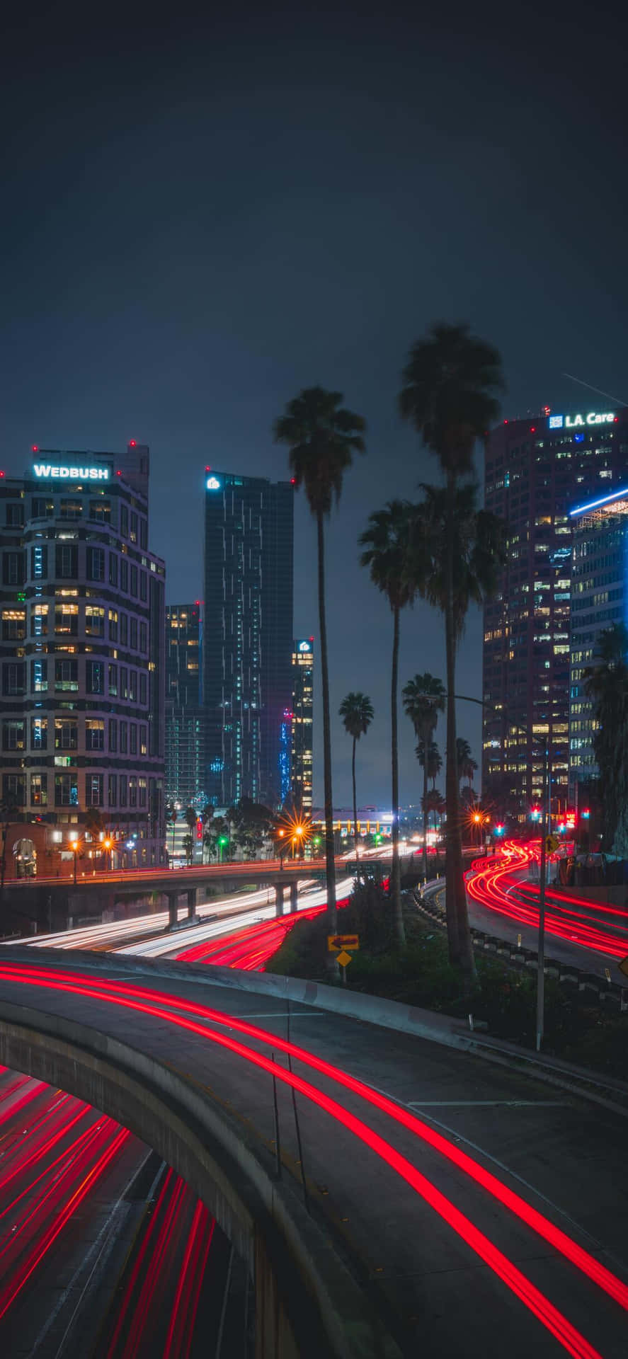 time lapse 桌布 壁紙 — 充滿活力的夜景，閃爍的摩天大樓和彎曲高速公路上的紅色車燈軌跡。