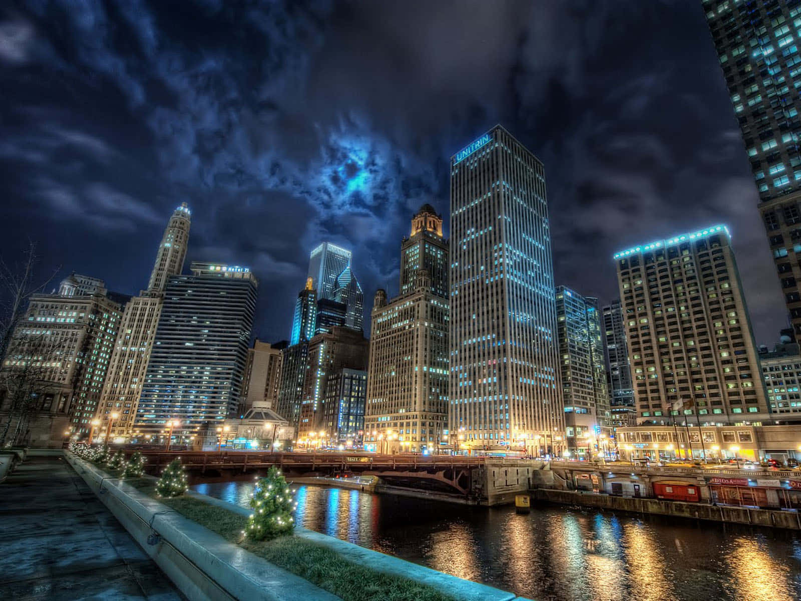 Beautiful City 桌布 壁紙 — 充滿活力的夜間城市景觀，在戲劇性的多雲天空下，燈火通明的摩天大樓倒映在河面上。
