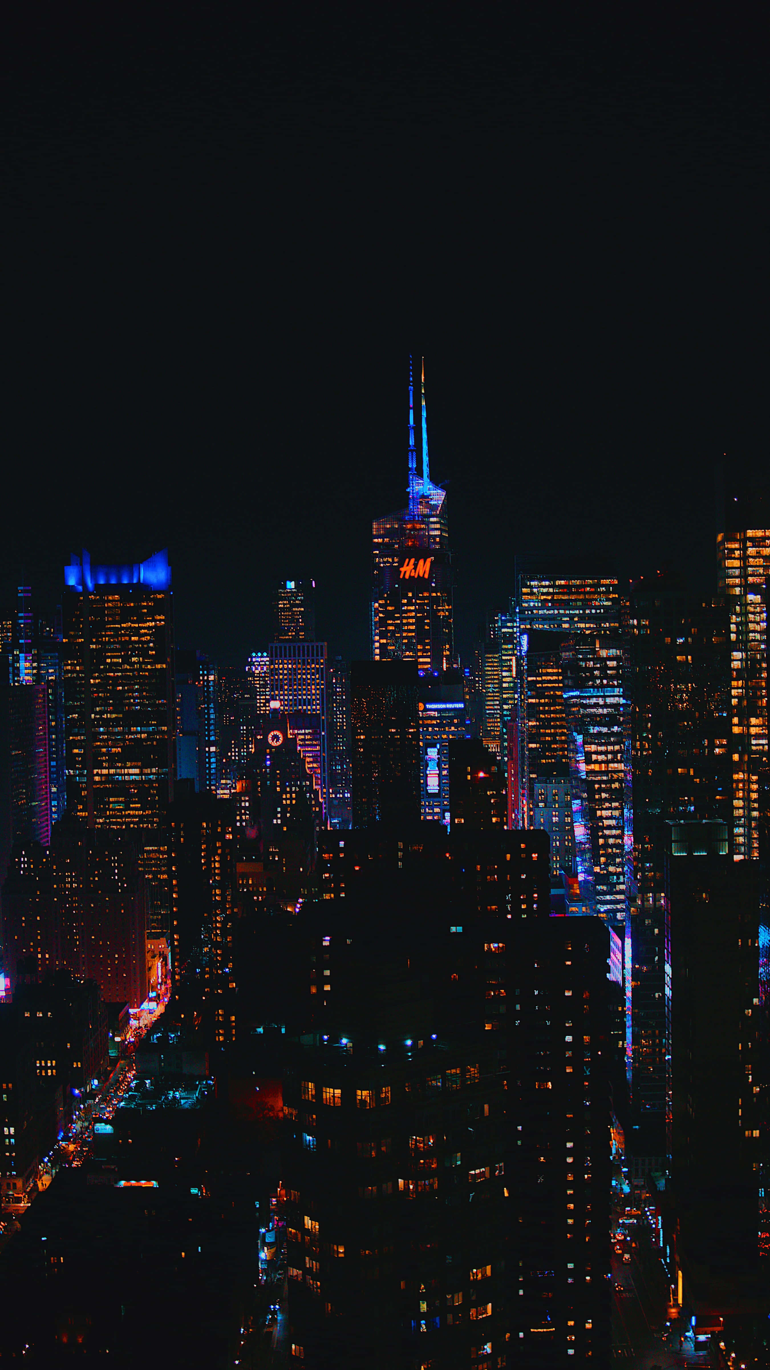 City Lights 桌布 壁紙 — 充滿活力的夜間城市景觀，高聳的摩天大樓在黑暗的天空中閃爍著五彩繽紛的霓虹燈光。