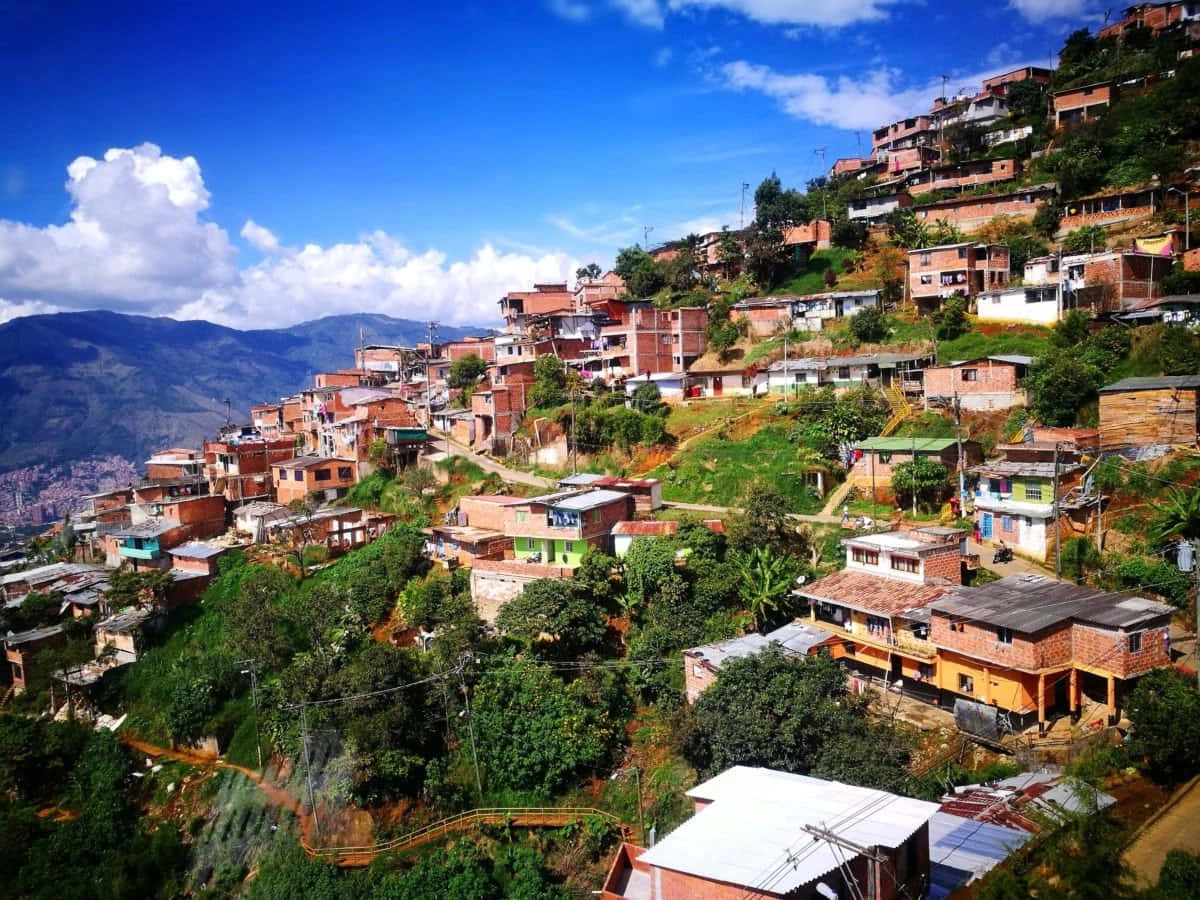 Colombia 桌布 壁紙 — 充滿活力的山坡村莊，梯田式的磚房坐落在茂密的綠植中，上方是晴朗的藍天和白雲。