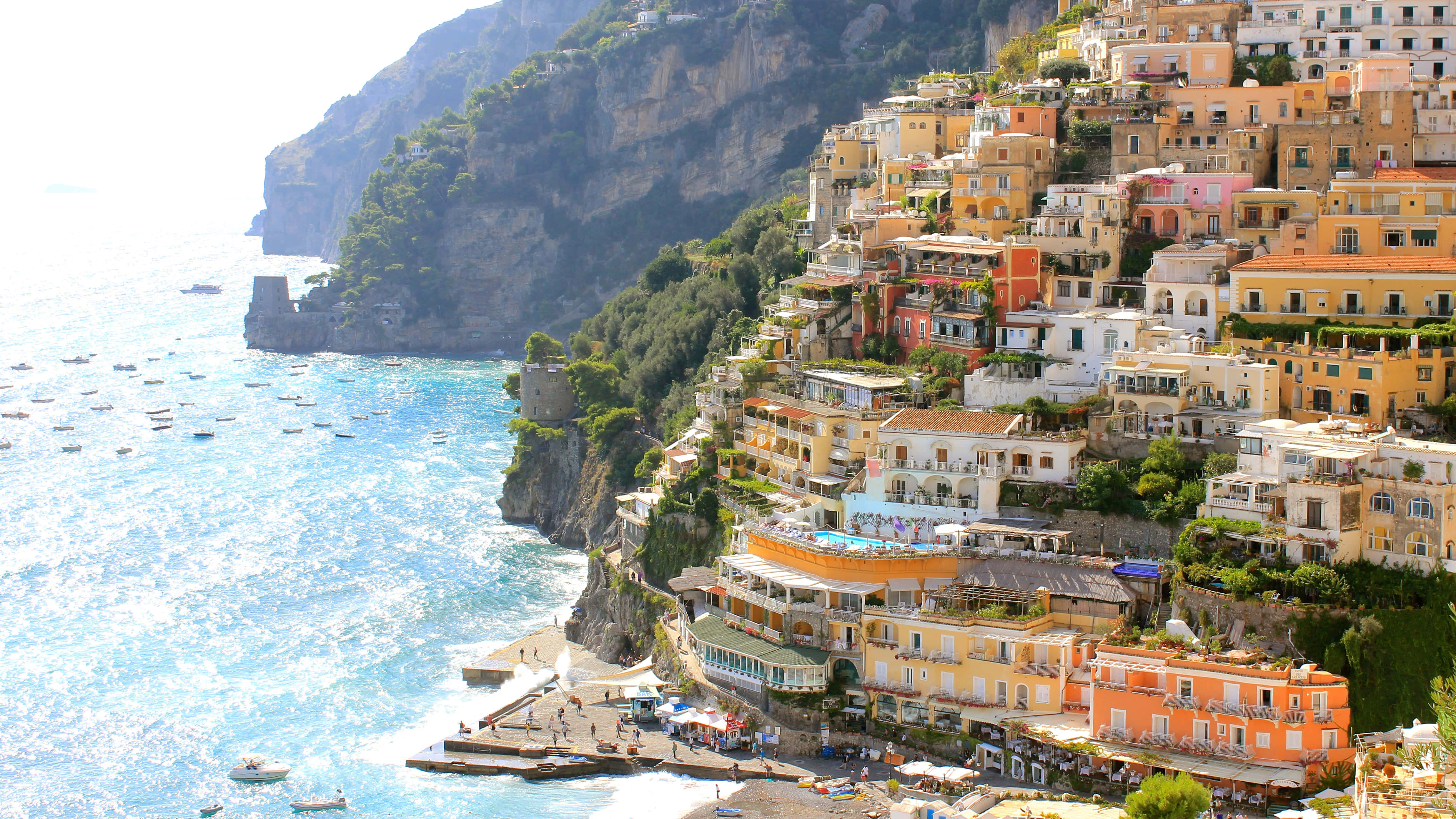 Italian Beach 桌布 壁紙 — 充滿活力的懸崖小鎮波西塔諾沿著陡峭的山坡層疊而下，流入點綴著船隻的碧綠海水，在明媚的陽光下閃耀。