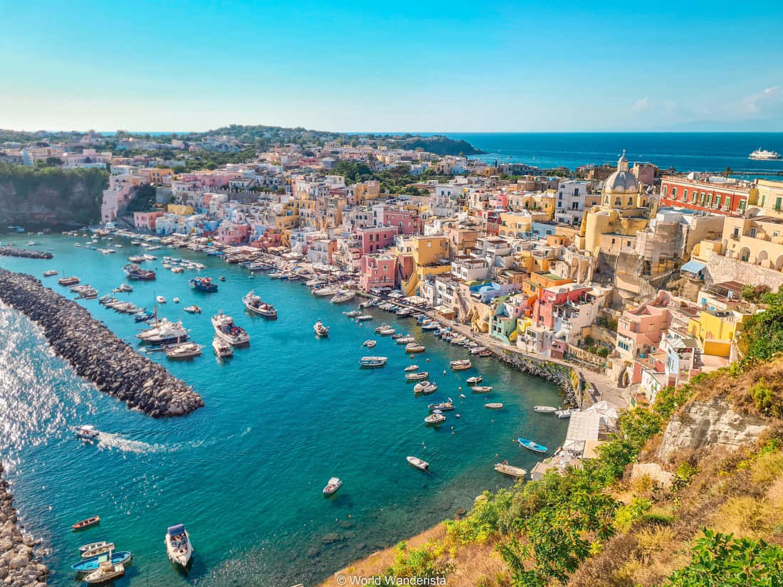 Italian Island 桌布 壁紙 — 充滿活力的懸崖村莊，粉彩建築和船隻在碧綠色的港口，藍天白雲。