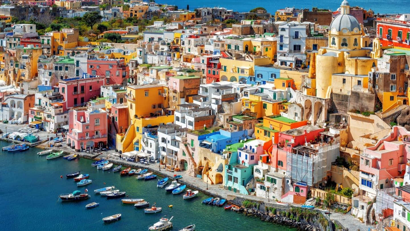 Italian Island 桌布 壁紙 — 充滿活力的懸崖村莊，粉彩房屋和船隻點綴在明亮的陽光下的碧綠海水上。