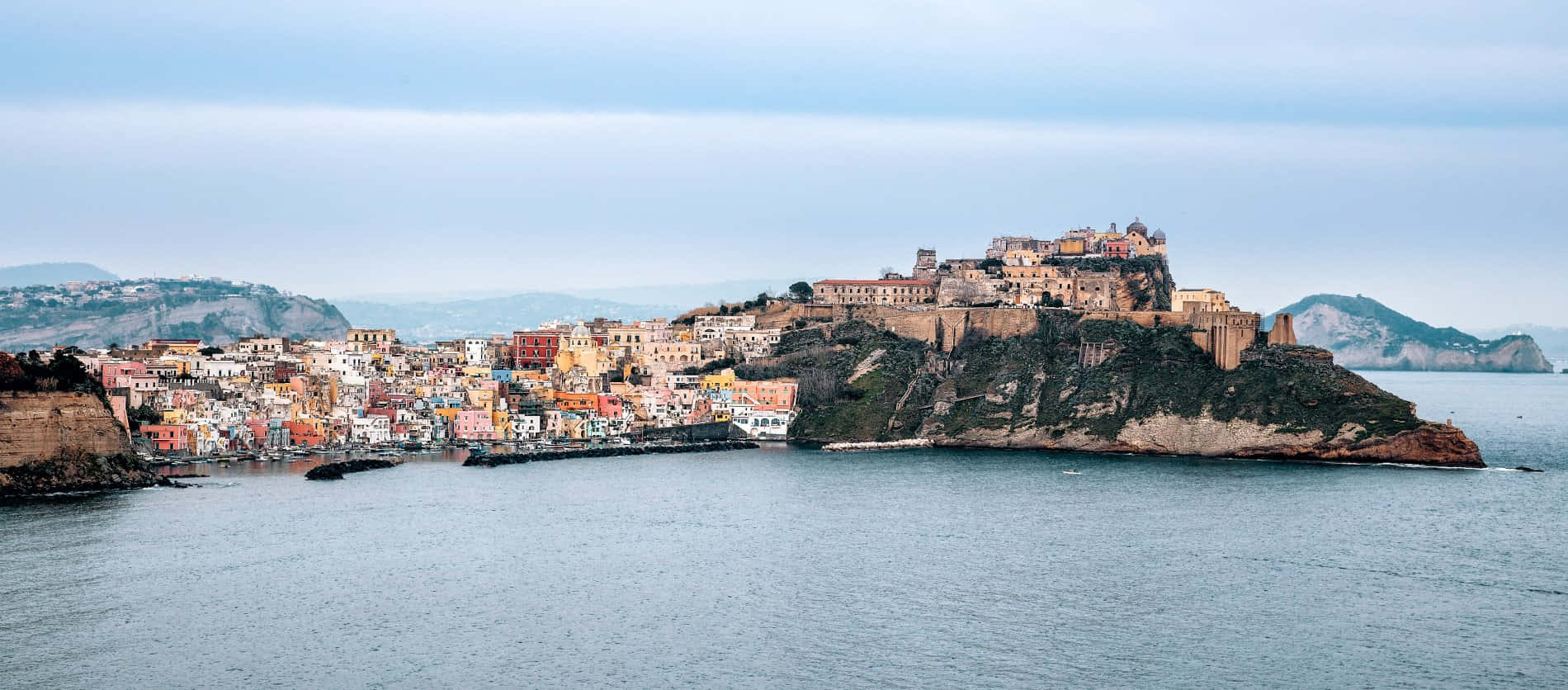 Italian Island 桌布 壁紙 — 充滿活力的懸崖村莊，色彩繽紛的房屋坐落在平靜的海面上，天空陰沉。