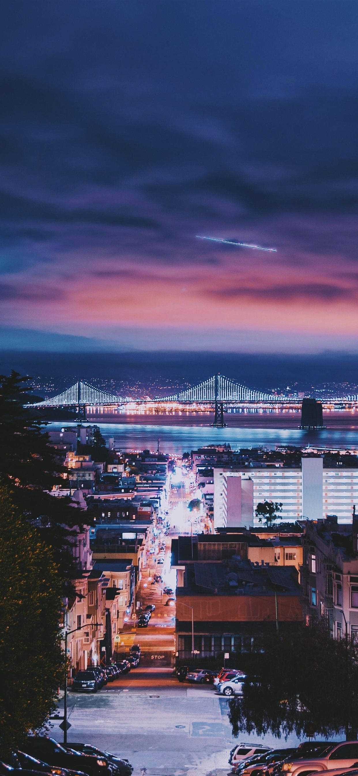 San Francisco Phone 桌布 壁紙 — 充滿活力的暮色城市景觀，特色是水面上發光的橋樑，下方是燈火通明的街道，天空呈現紫色和粉紅色。