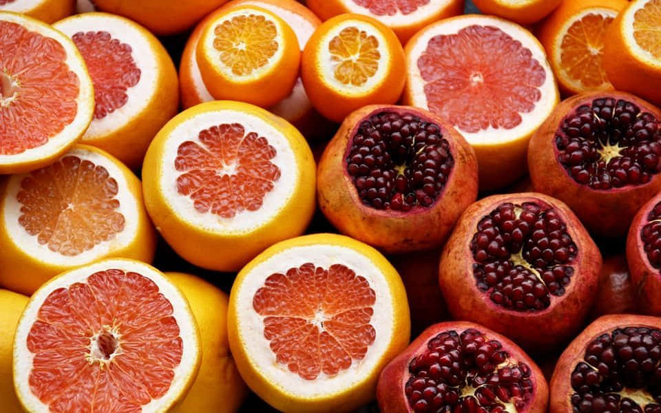 Winter Fruits 桌布 壁紙 — 充滿活力的柑橘類水果（包括西柚和石榴）切半特寫，展現多汁的果肉和種子。