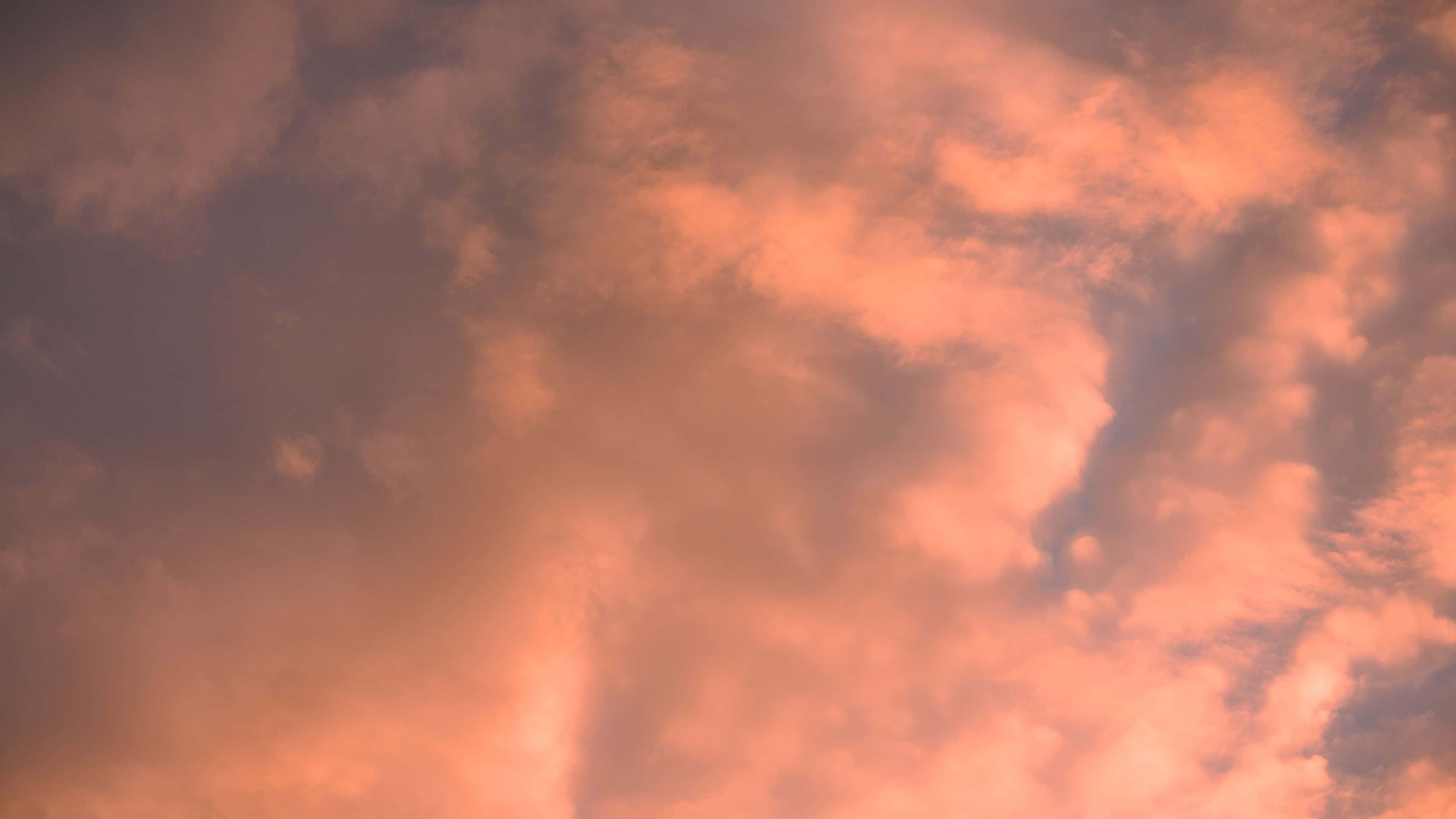 唯美雲朵動態 桌布 壁紙 — 充滿活力的橙色和粉紅色雲朵在暮色天空中戲劇性地旋轉，帶有柔和漸變和紋理縷縷。