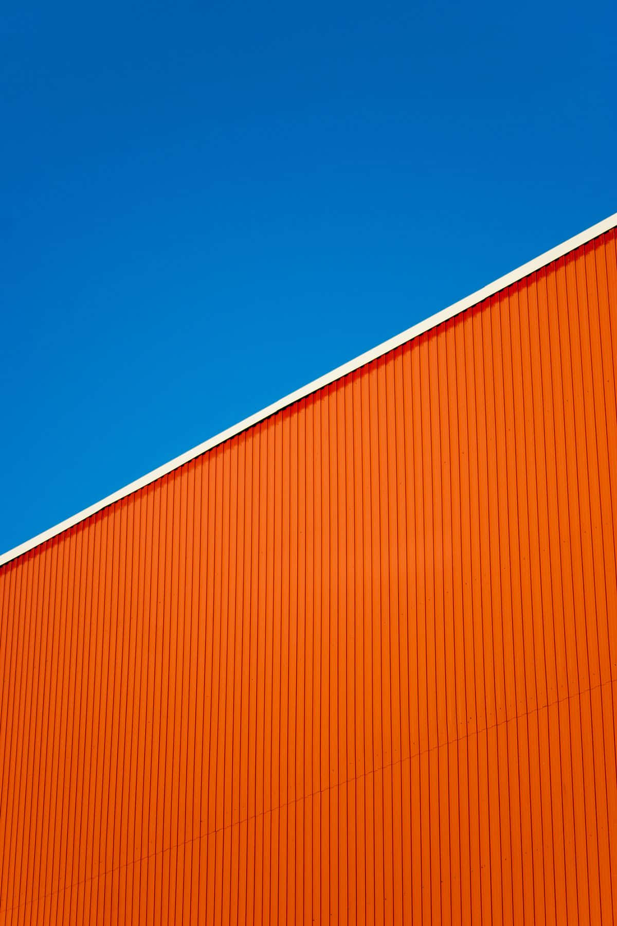 Minimalist Photography 桌布 壁紙 — 充滿活力的橙色波紋牆以對角線切割清澈的藍天，形成大膽的幾何構圖。