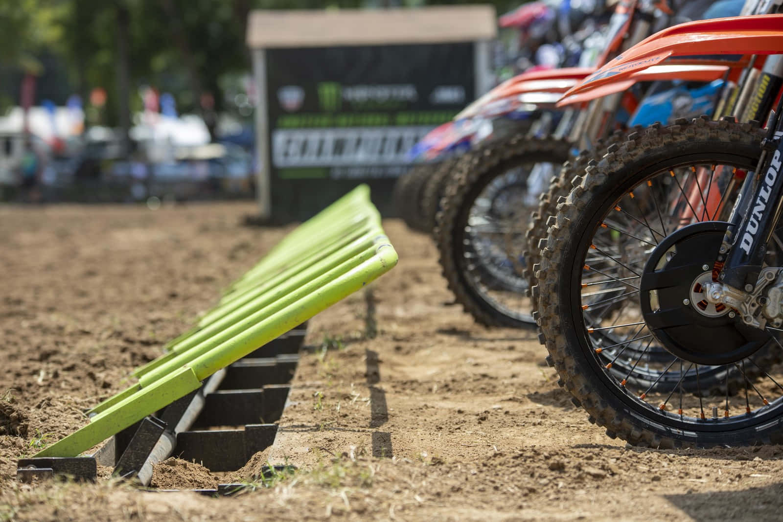 Dirtbike 桌布 壁紙 — 充滿活力的橙色越野電單車在泥地上排成一列的近景，前景有亮綠色障礙物。