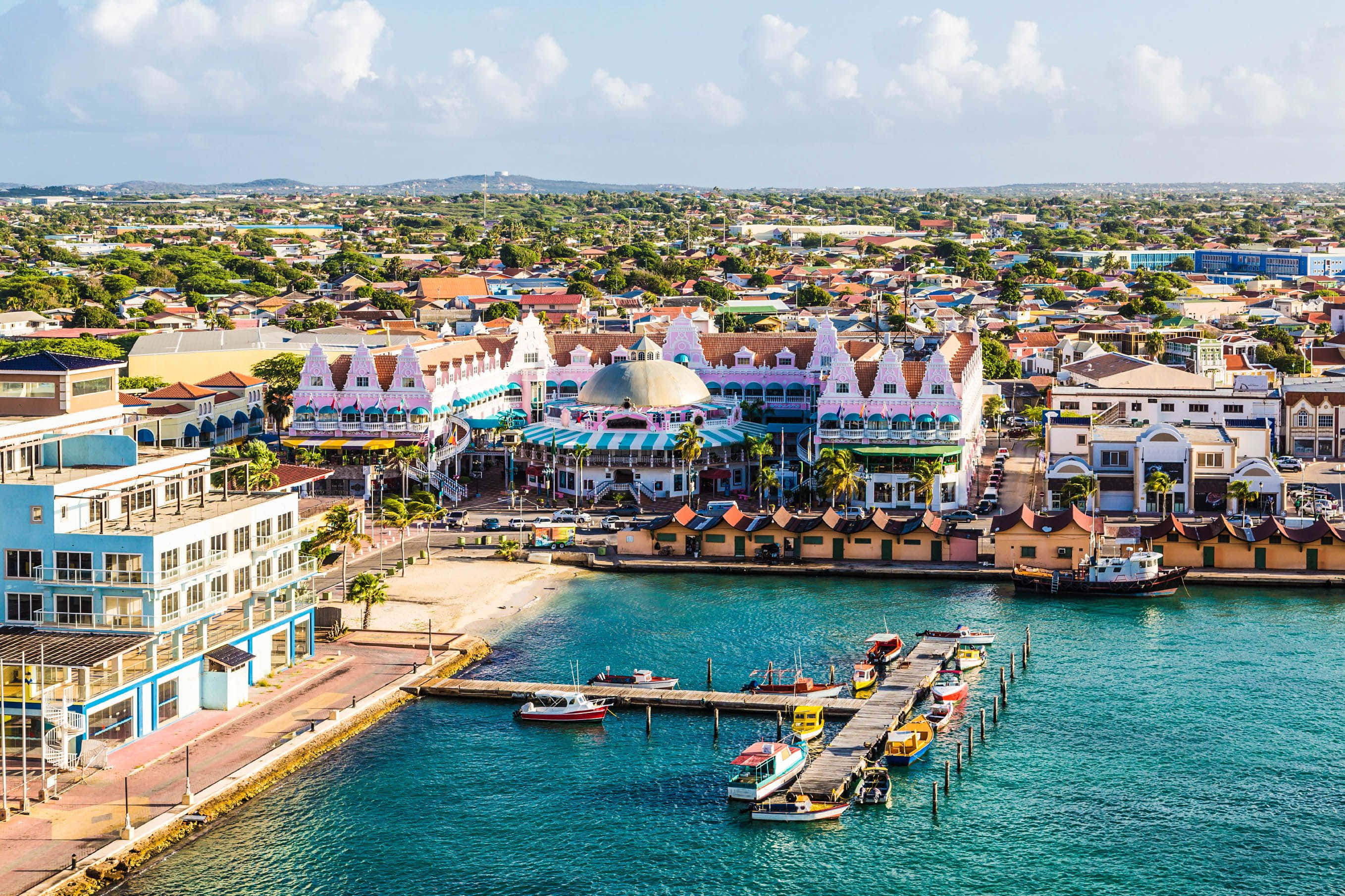 Aruba 桌布 壁紙 — 充滿活力的沿海小鎮鳥瞰圖，擁有色彩繽紛的建築物、碧綠的海水以及停泊在碼頭的船隻，天空湛藍明亮。